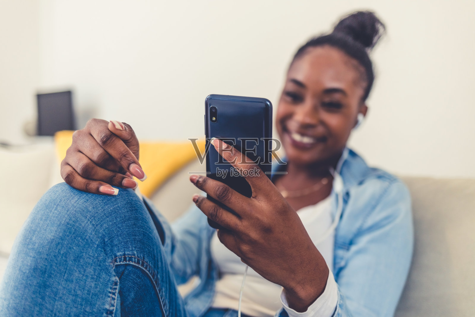 一个年轻的非洲妇女在家里使用电话的特写。Shot of a young women wearing headphones to listen to music on her cellphone.照片摄影图片