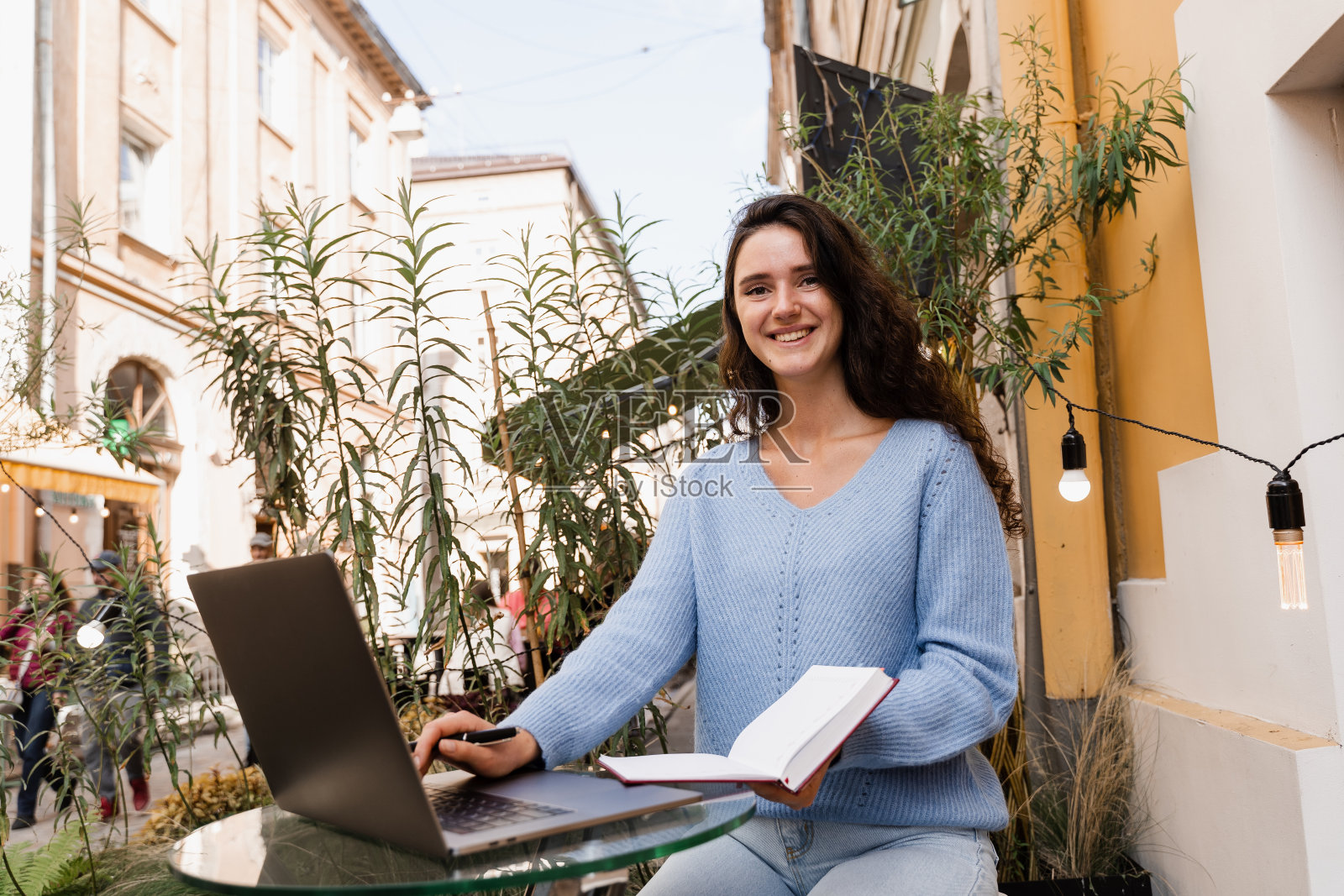 迷人的年轻女子有视频交流课与老师在外面。聪明的女孩学生用笔记本电脑在线学习英语，并在咖啡馆的语言学校写笔记。照片摄影图片