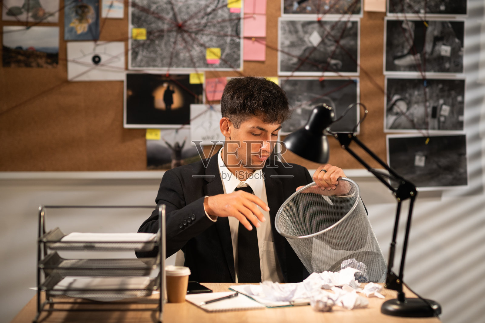 侦探在办公室工作，在办公桌前揉皱纸张，把它扔进垃圾桶，废纸扔进垃圾筐照片摄影图片