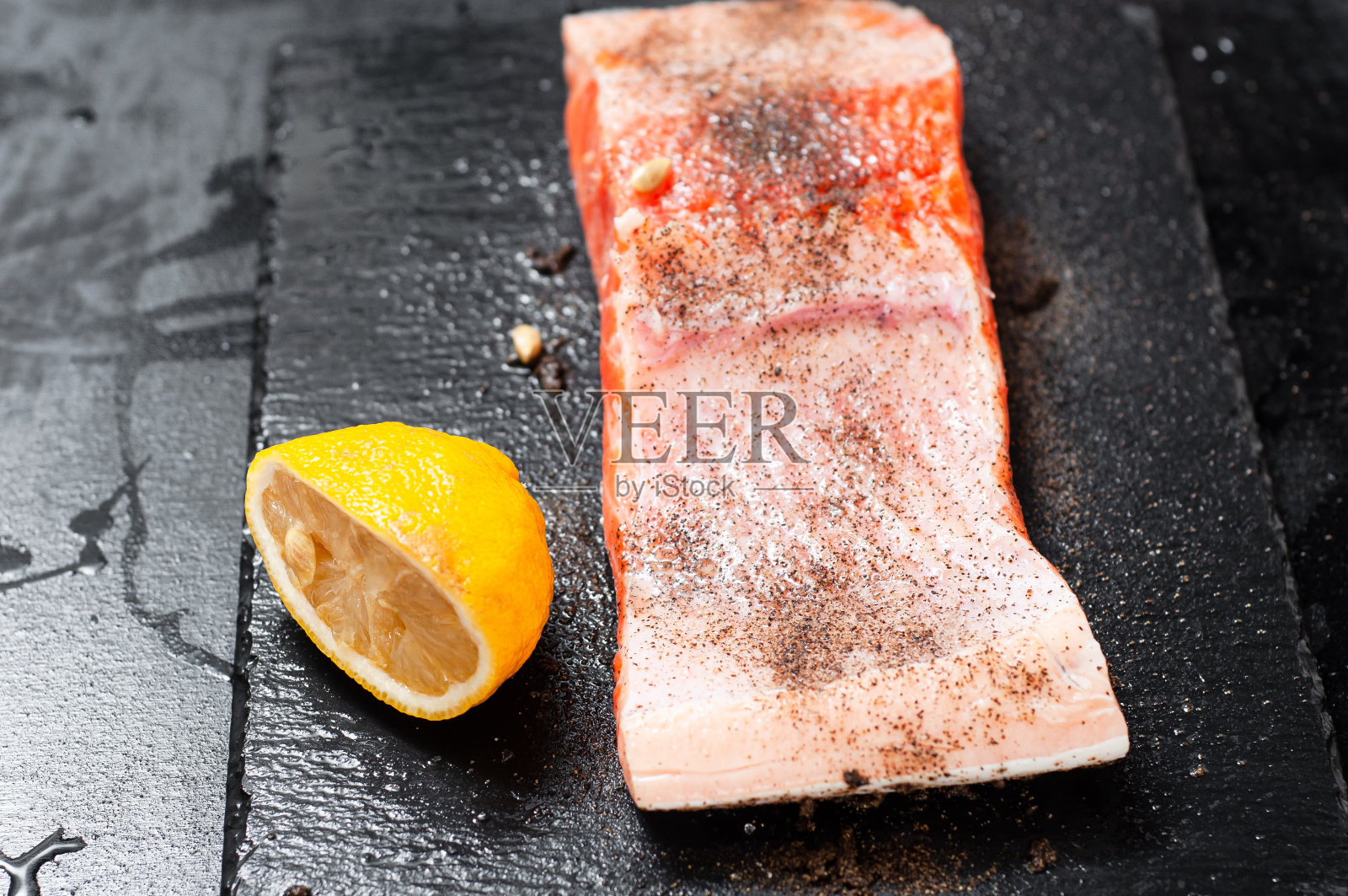 用胡椒和盐调味的三文鱼片放在石制的架子上，旁边放着挤好的柠檬汁照片摄影图片