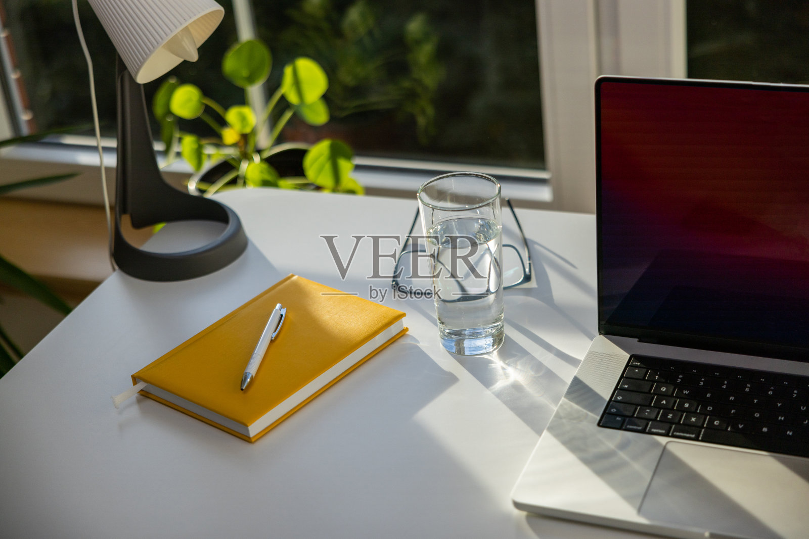 笔记本电脑，黄色的个人记事本，眼镜和盛水的玻璃杯放在桌上照片摄影图片