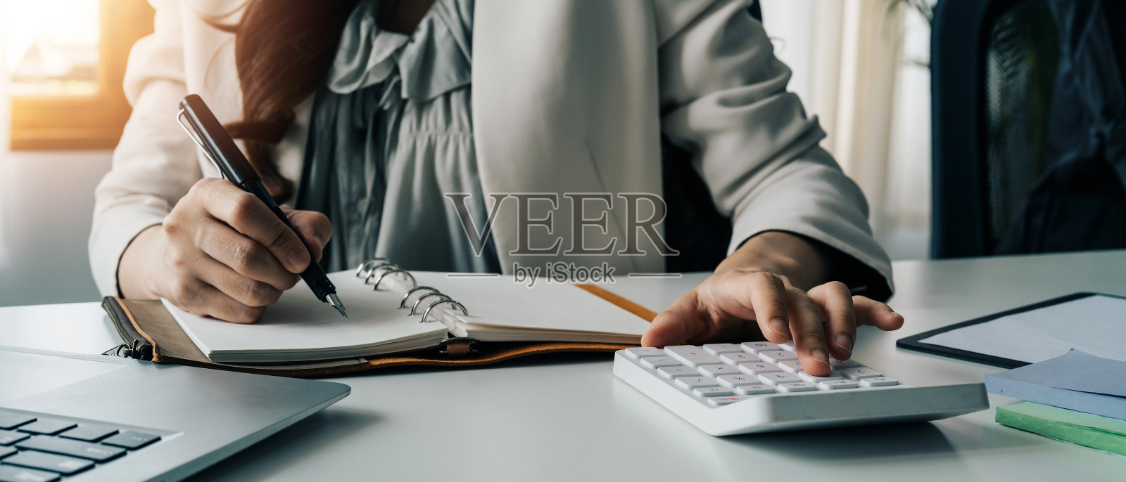 女会计在工作场所一边使用计算器一边在纸上写信息。办公室的概念照片摄影图片