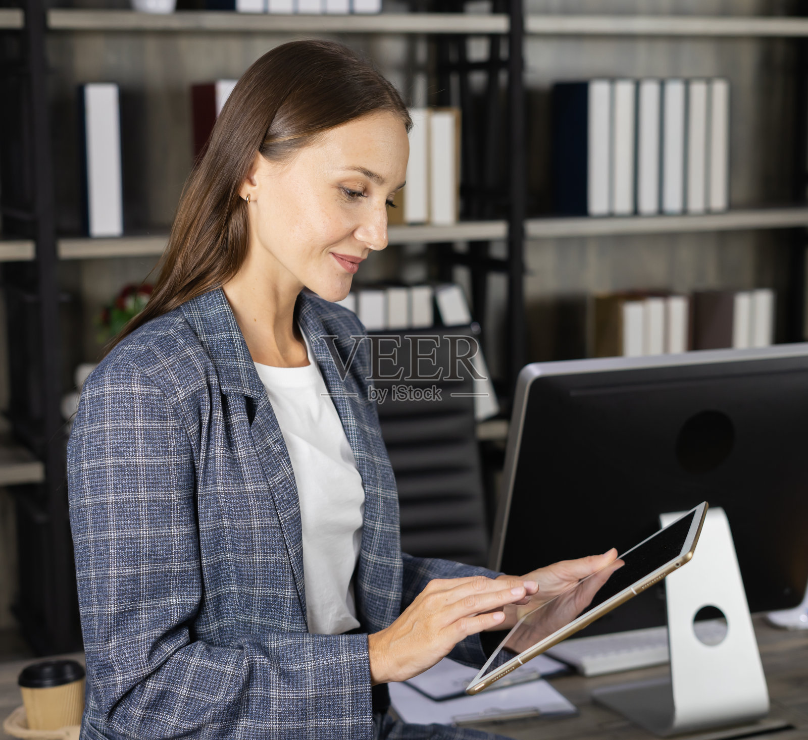 聪明的女商人穿着西装，在工作场所使用平板电脑。美丽的年轻女性看起来像女商人或工人或秘书在公司办公室工作照片摄影图片