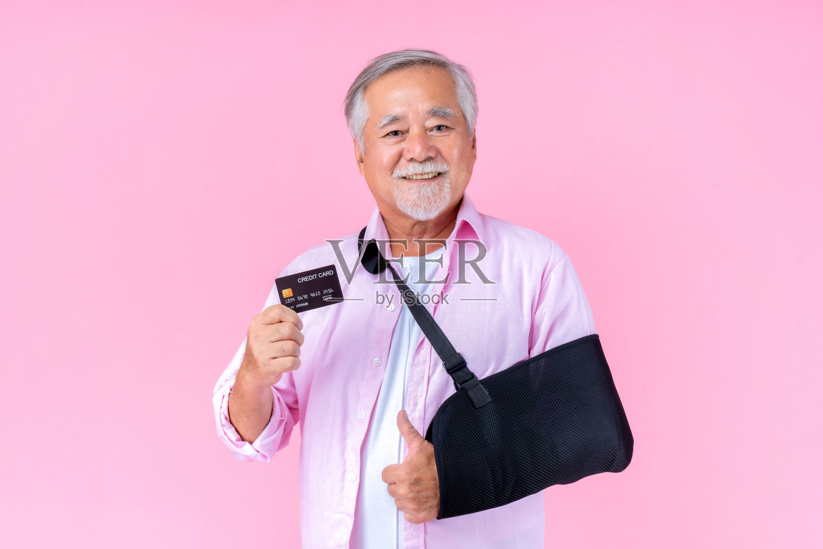 旅行退休的亚洲老人戴着帽子，手臂骨折，戴着夹板进行治疗，微笑着，手持信用卡进行自信的生活方式，老年男性支付信用卡医疗。照片摄影图片