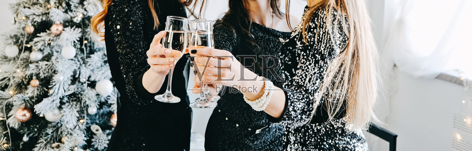 干杯，用香槟干杯。朋友们庆祝圣诞节或新年前夜的聚会。一群人用香槟杯欢呼，背景是节日的内部照片摄影图片