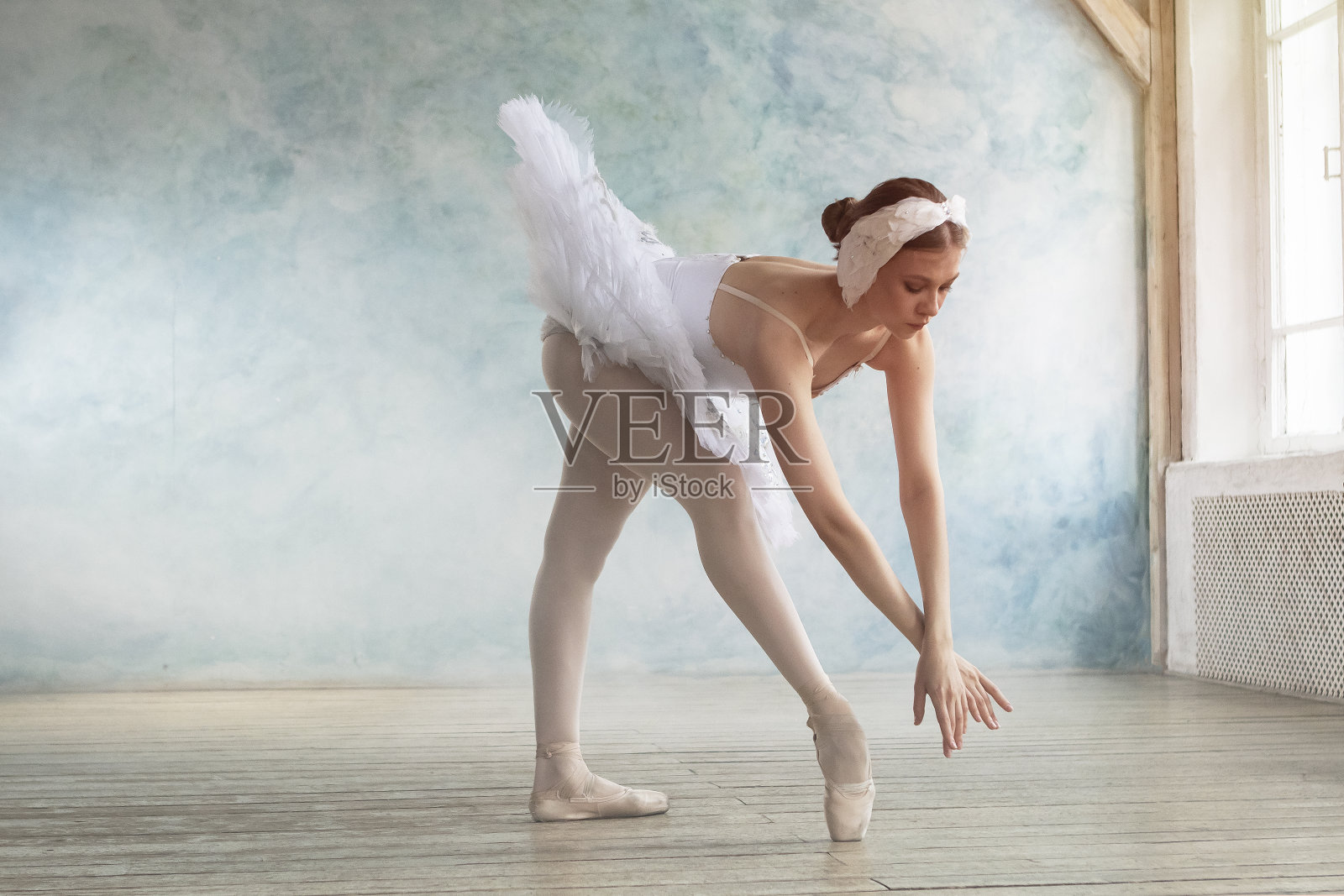 一名穿着白色芭蕾舞裙的职业芭蕾舞演员在有蓝色墙壁和烟雾的房间里跳舞照片摄影图片