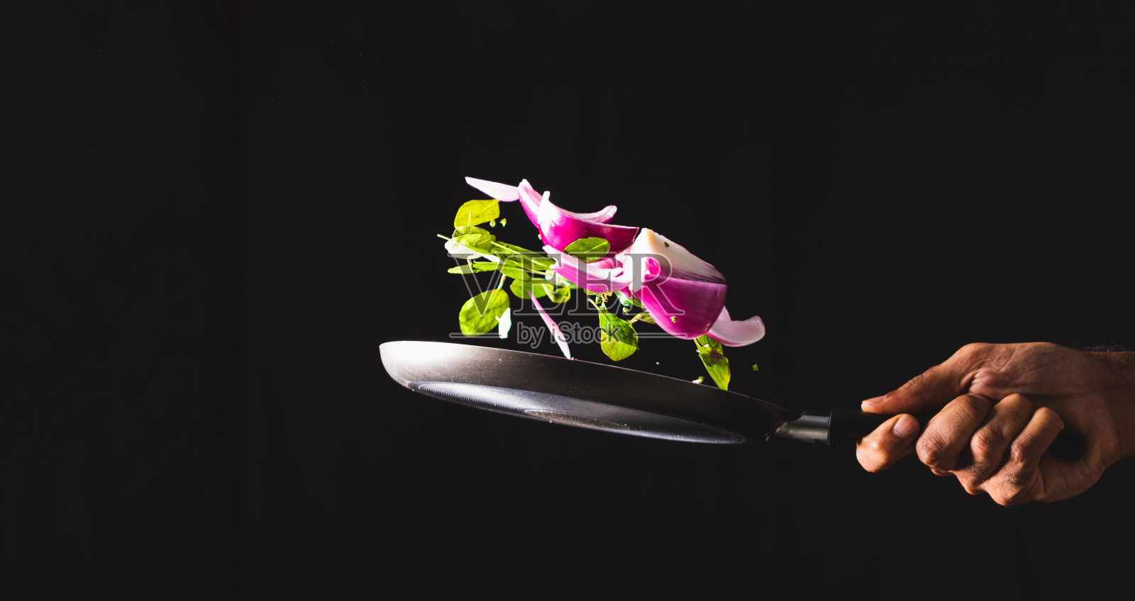 煎锅把红洋葱、奶酪、罗勒和调味料扔到空中。照片摄影图片