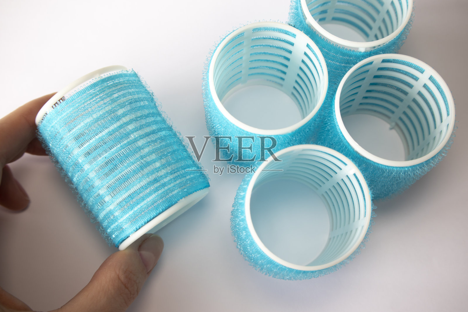 女人手里拿着蓝色的魔术贴卷发器。照片摄影图片