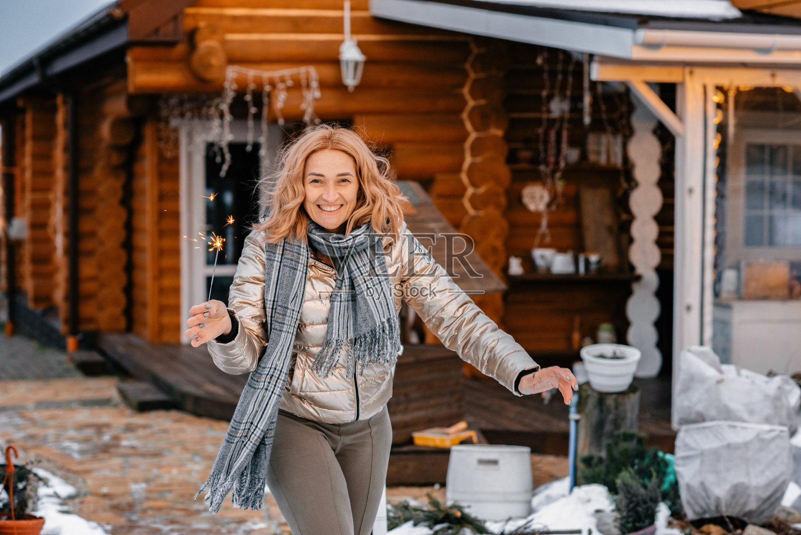 快乐的金发女孩在雪地里奔跑，手里拿着烟花。幸福和有趣的概念。下雪的乡村房子。照片摄影图片