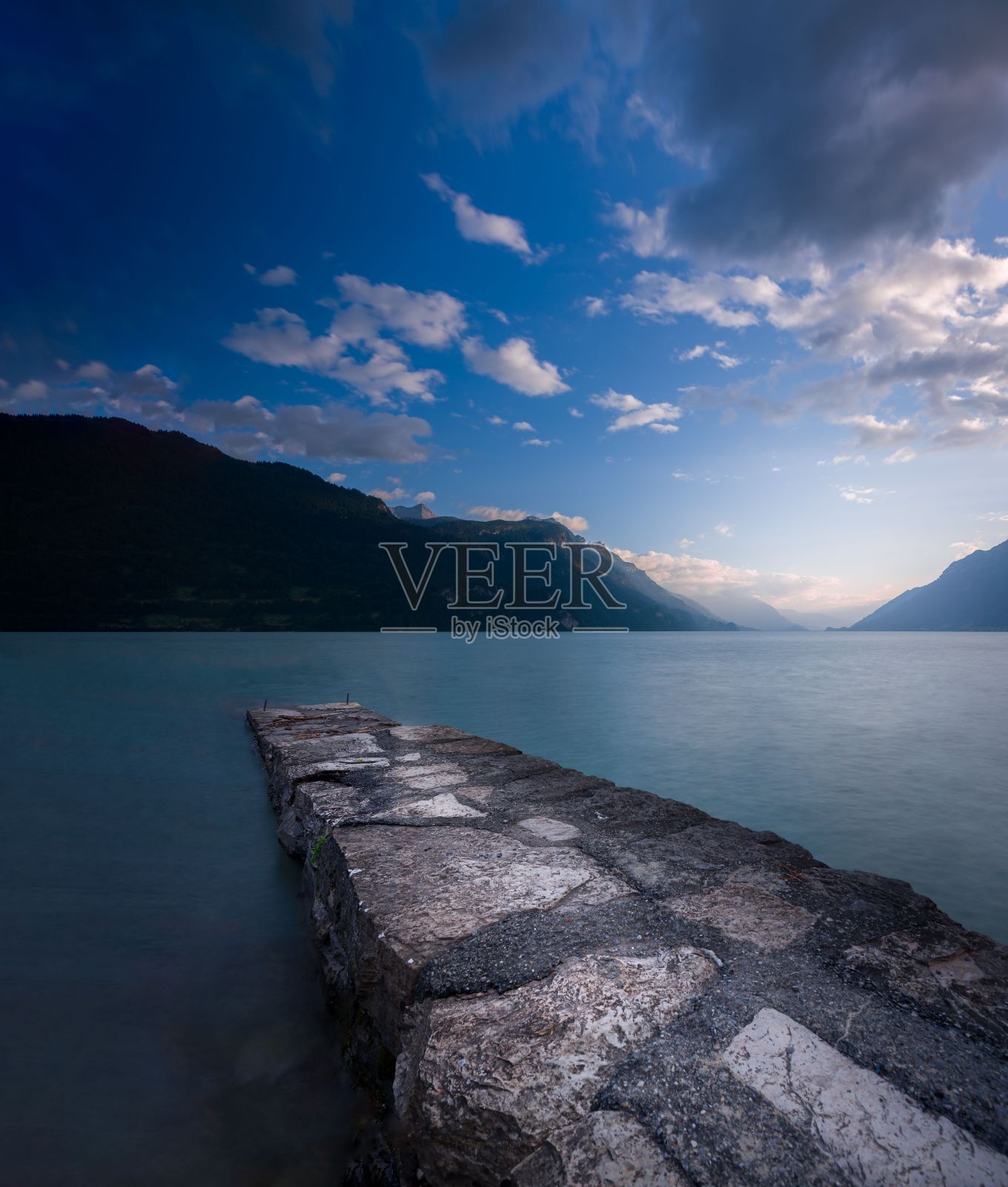 在多云的蓝天下，俯瞰群山的湖面上的码头的垂直镜头照片摄影图片