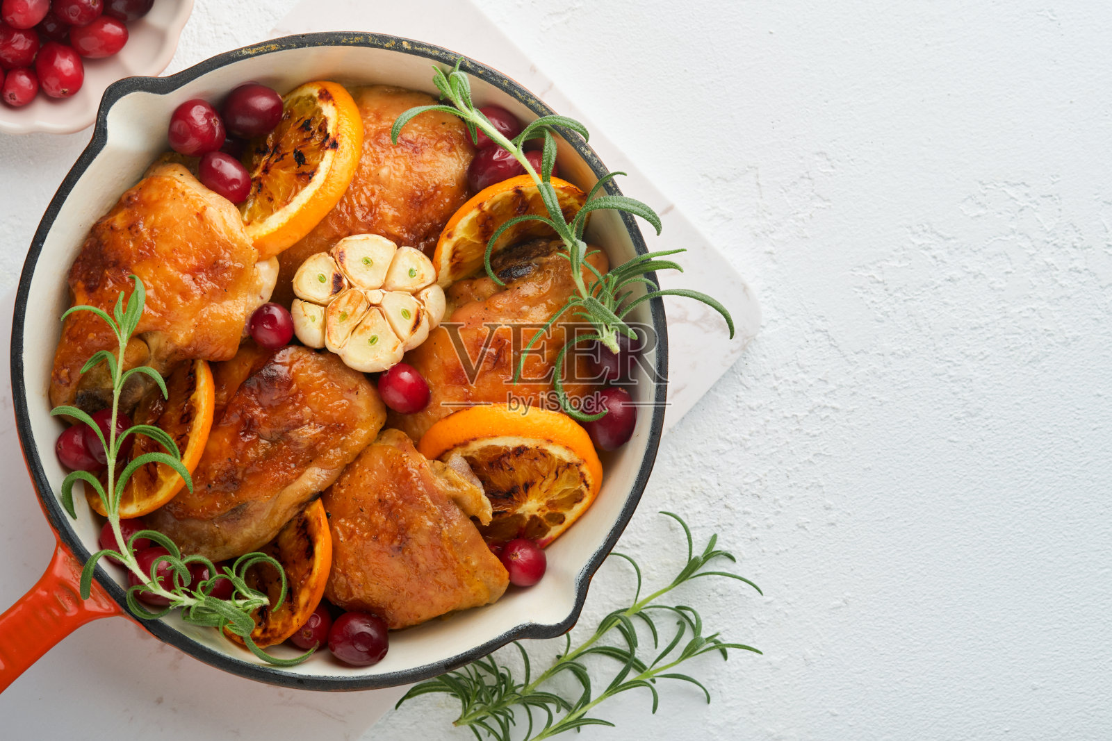 烤鸡腿配橙汁、蔓越莓和香辣香草迷迭香，盛于平底锅中。节日圣诞晚餐概念菜单。前视图。本空间照片摄影图片