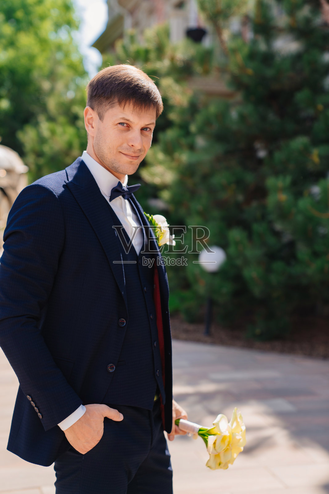 新郎穿着深蓝色的西装，上面有一枚胸花和一束马蹄莲。照片摄影图片