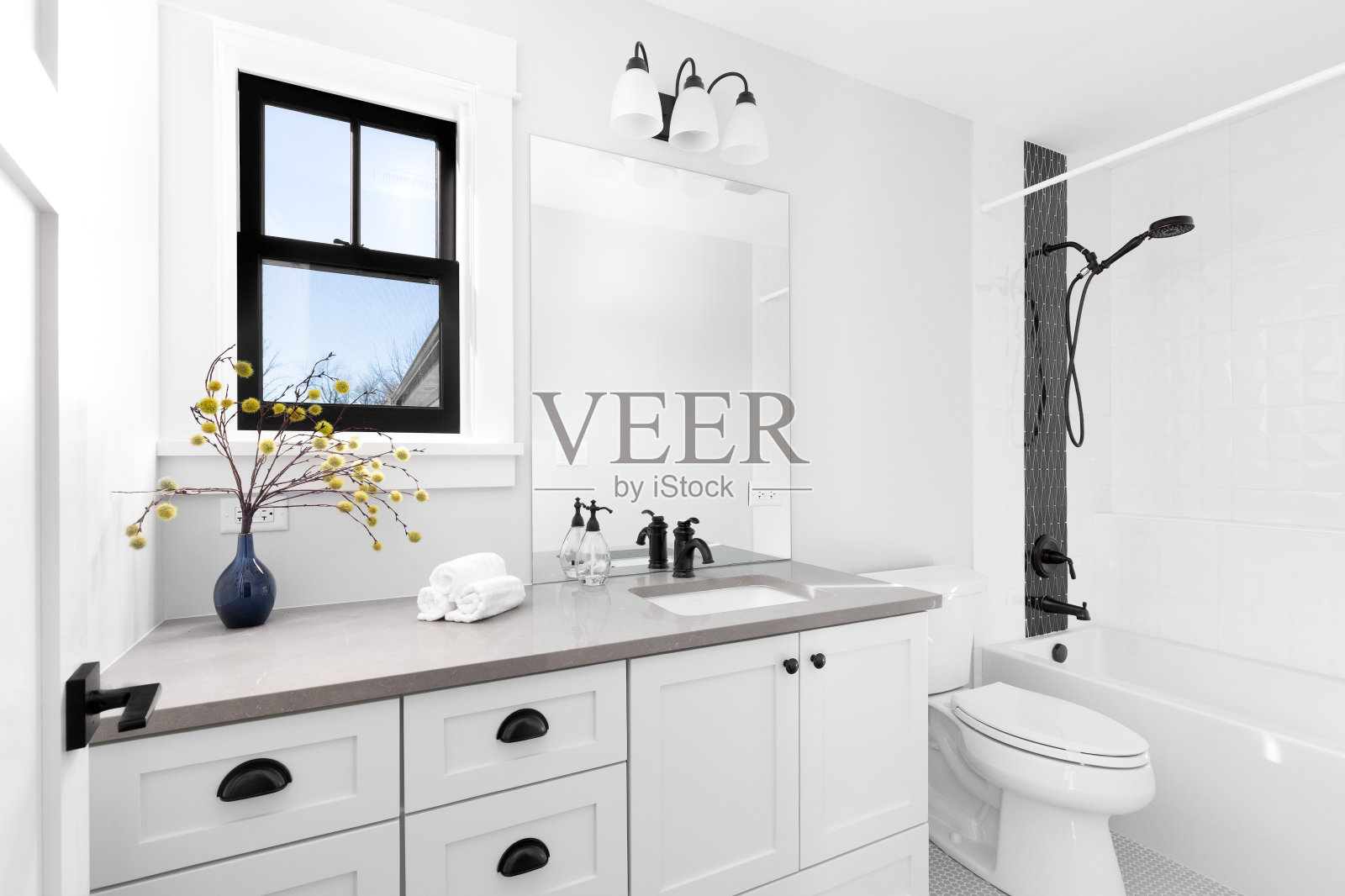 一间带有灰色花岗岩台面和瓷砖淋浴的白色浴室。照片摄影图片