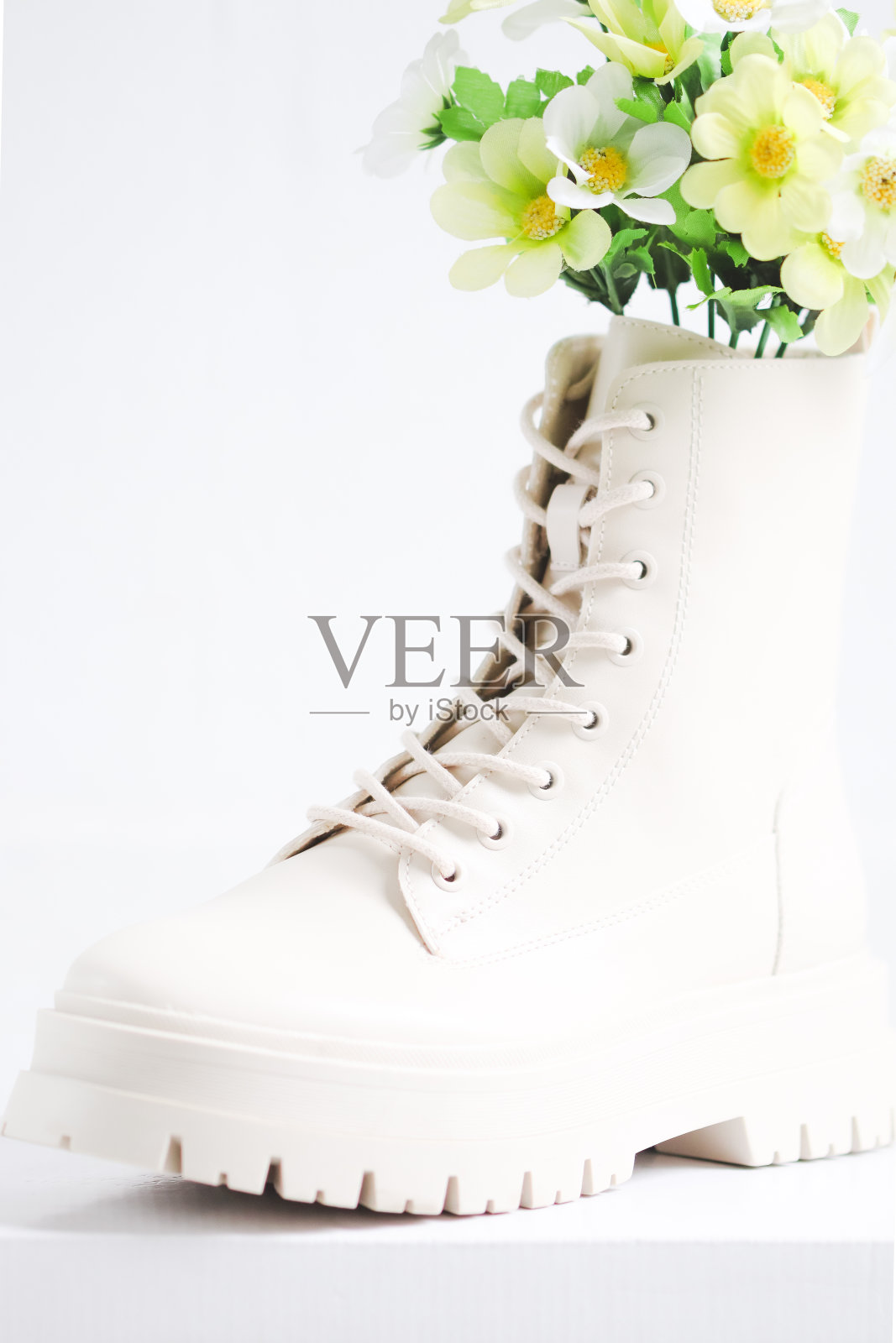 白色的纸板箱上放着一只白色的鞋子，鞋底粗糙，有鞋带，上面放着一束花。照片摄影图片