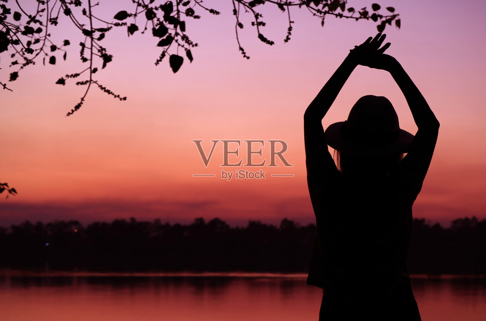 在紫色和粉色渐变的湖边放松的戴帽子女士剪影照片摄影图片