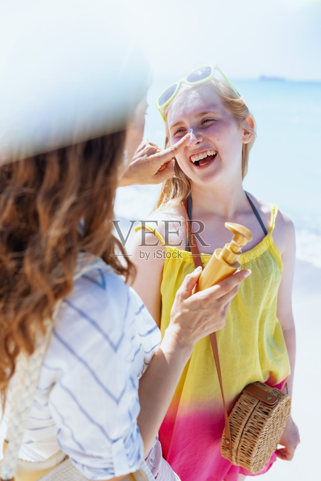 快乐的母亲和十几岁的女儿在海滩上涂防晒霜照片摄影图片