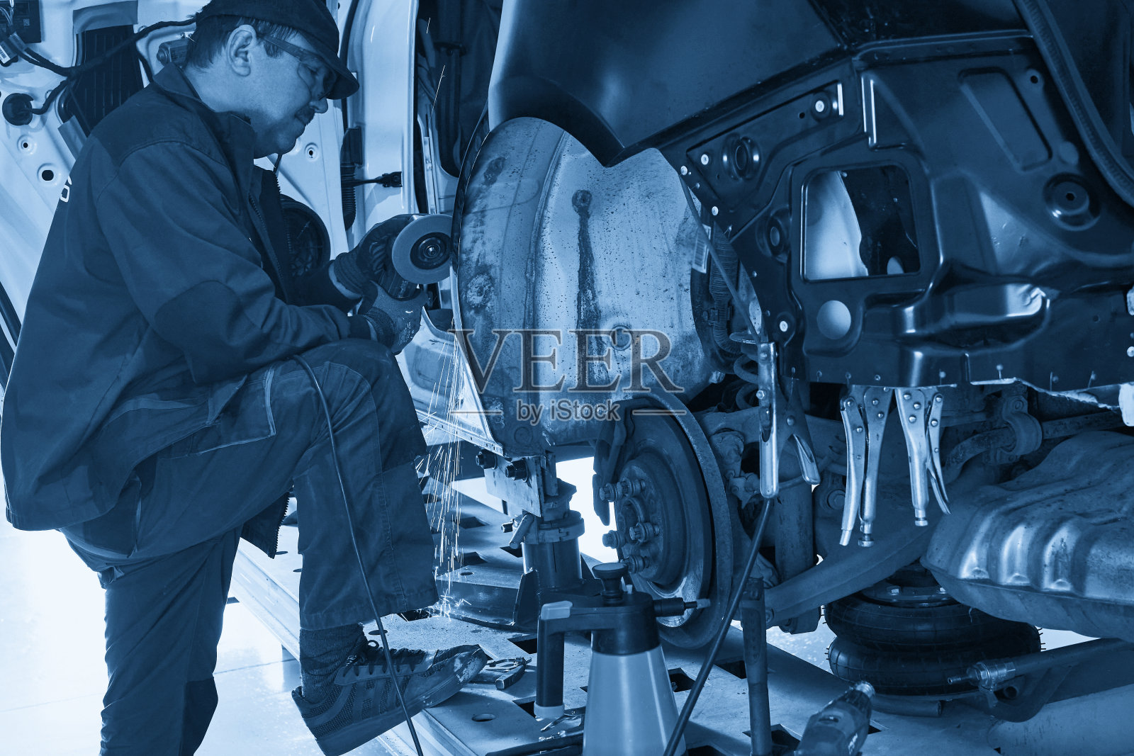 修理服务人员修理损坏的汽车。用角磨床固定金属体。照片摄影图片