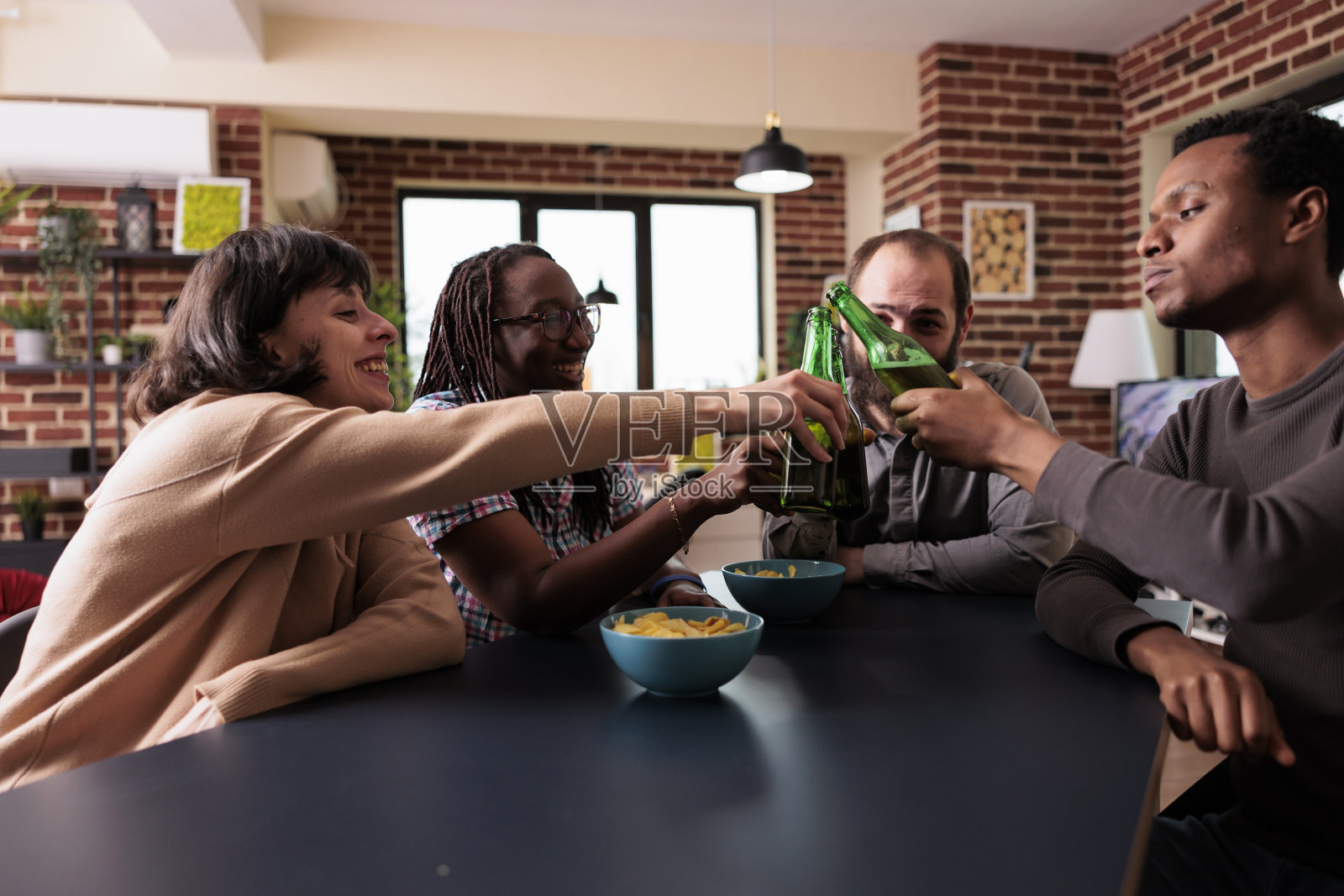 各式各样的朋友在家里用点心和啤酒庆祝团聚。照片摄影图片