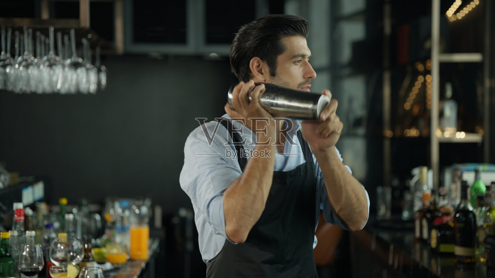 调酒师工作技能，年轻调酒师调制鸡尾酒在鸡尾酒吧，调酒师站在吧台，手里拿着摇酒器照片摄影图片