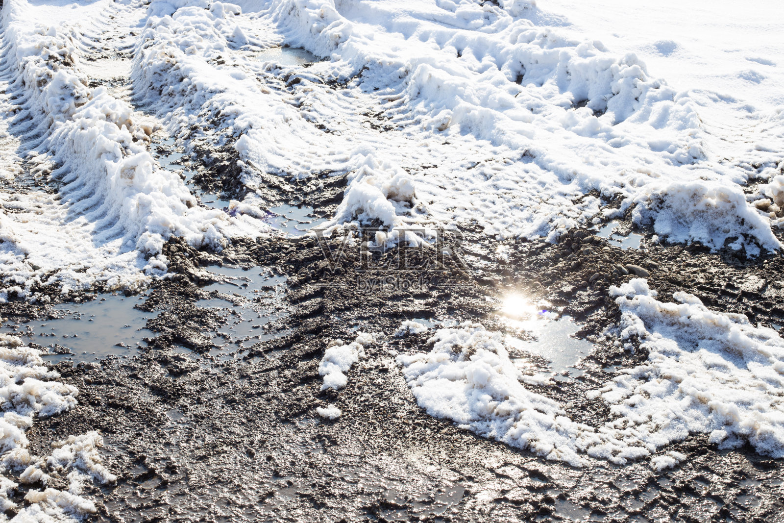 在明亮的阳光照射下，土路上融化的雪和汽车轮胎印照片摄影图片