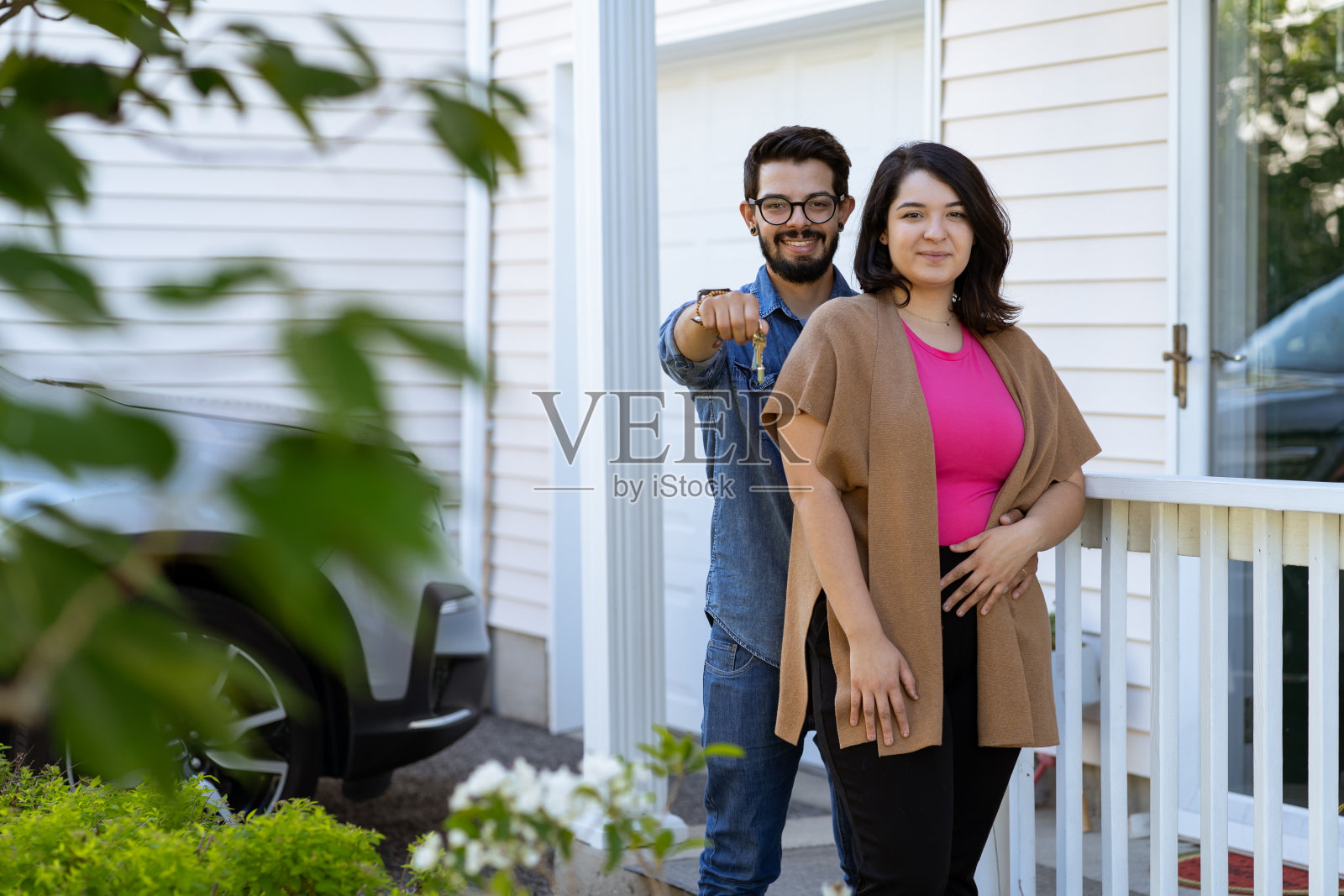 一对年轻的拉丁夫妇在他们的新房子前拿着钥匙照片摄影图片