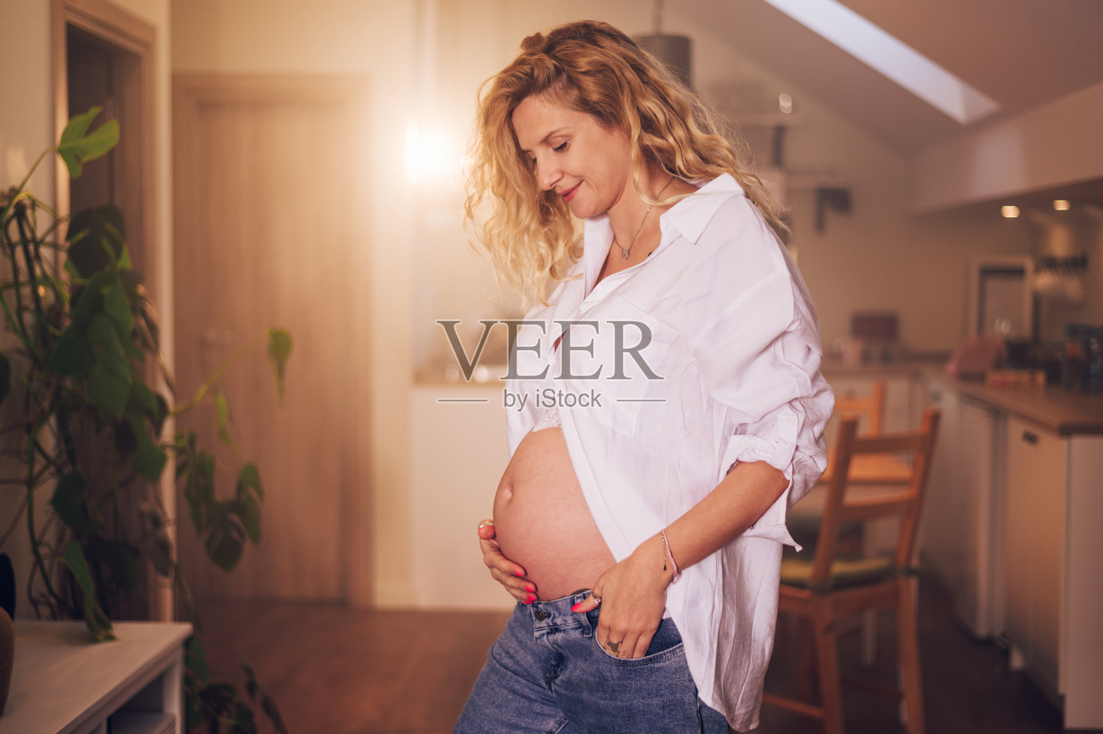 孕妇站在家里的肖像，手放在她的肚子上照片摄影图片