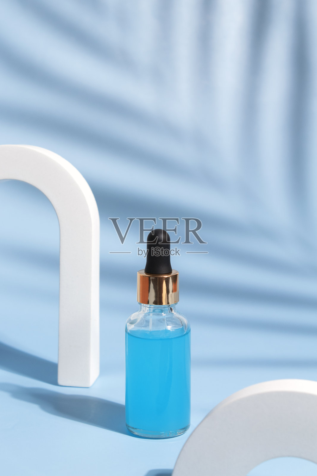 用玻璃滴管将化妆品油、精华液或精华液放在蓝色背景上，上面有棕榈叶的阴影。草药顺势疗法产品。天然有机温泉化妆品。照片摄影图片