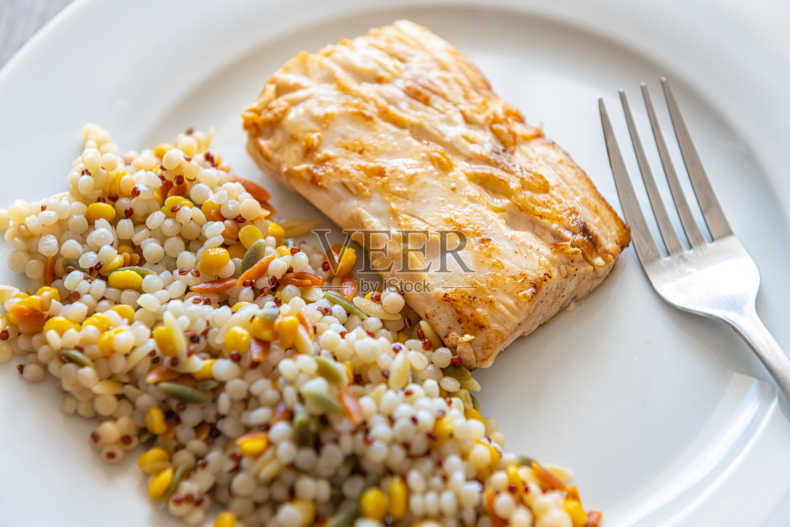 微距特写mahi mahi鱼海鲜用叉子在白色盘子上煮熟的鱼片，由蒸粗麦粉意大利面，裂鹰嘴豆和红藜麦混合而成照片摄影图片