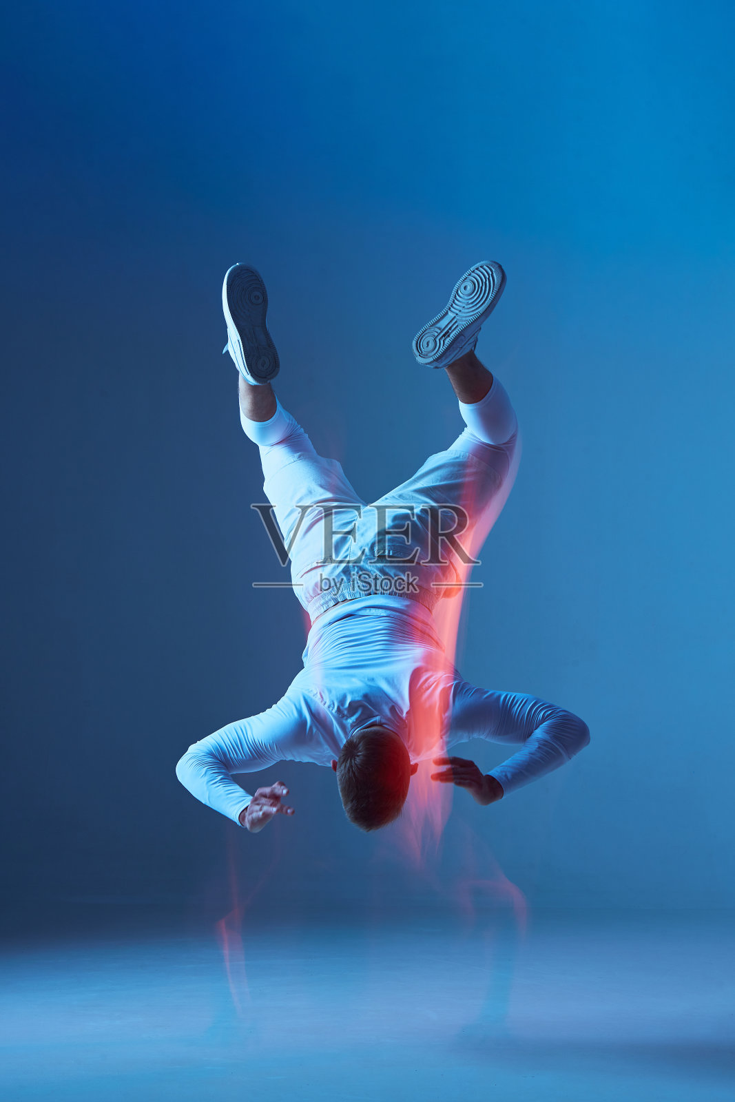 职业男性运动员的肖像，运动员训练在工作室，做跳高颠倒在蓝色背景。照片摄影图片
