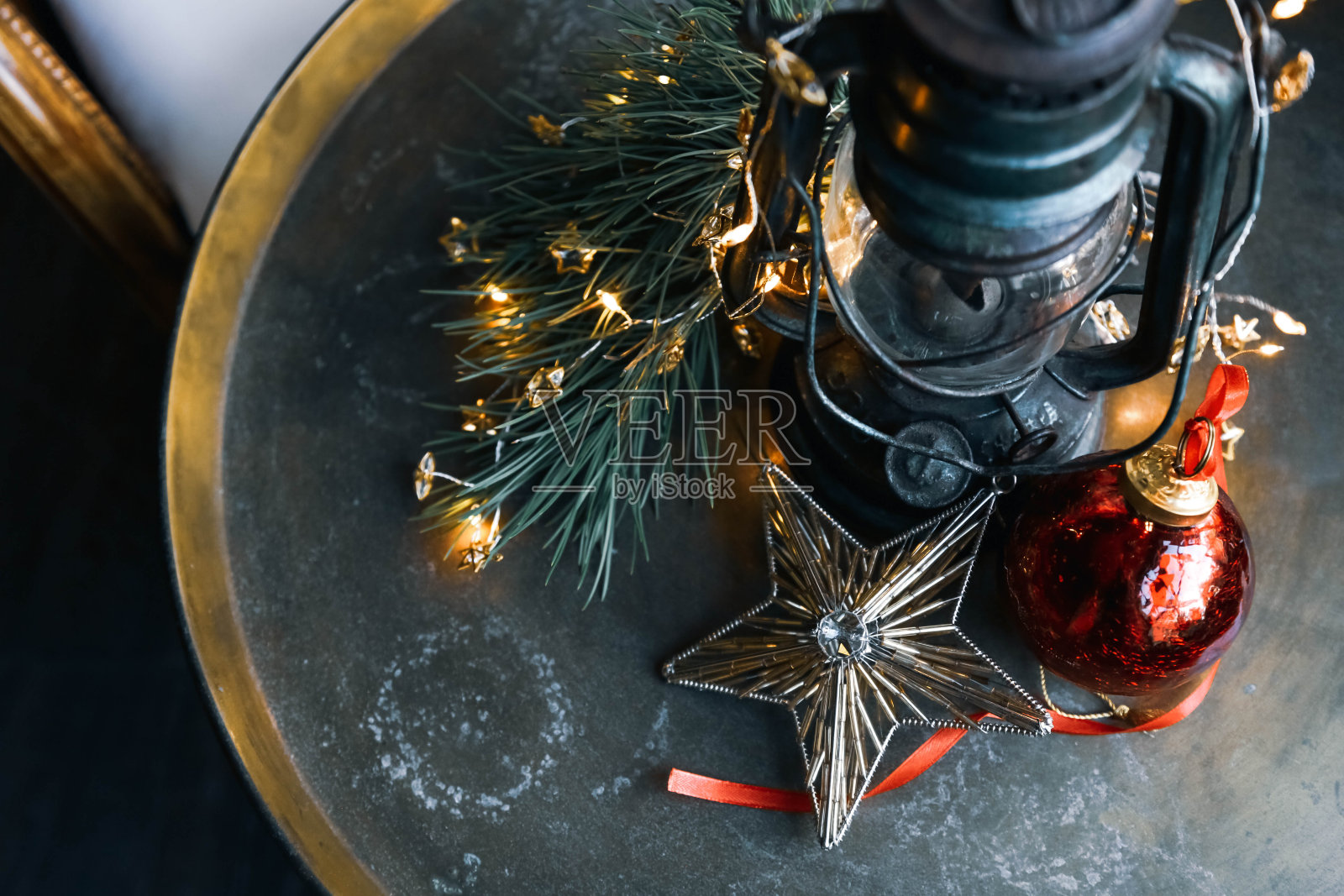 一盏古色古香的台灯、一颗玻璃做成的星星和其他漂亮的圣诞装饰品放在一张圆铜桌上。照片摄影图片