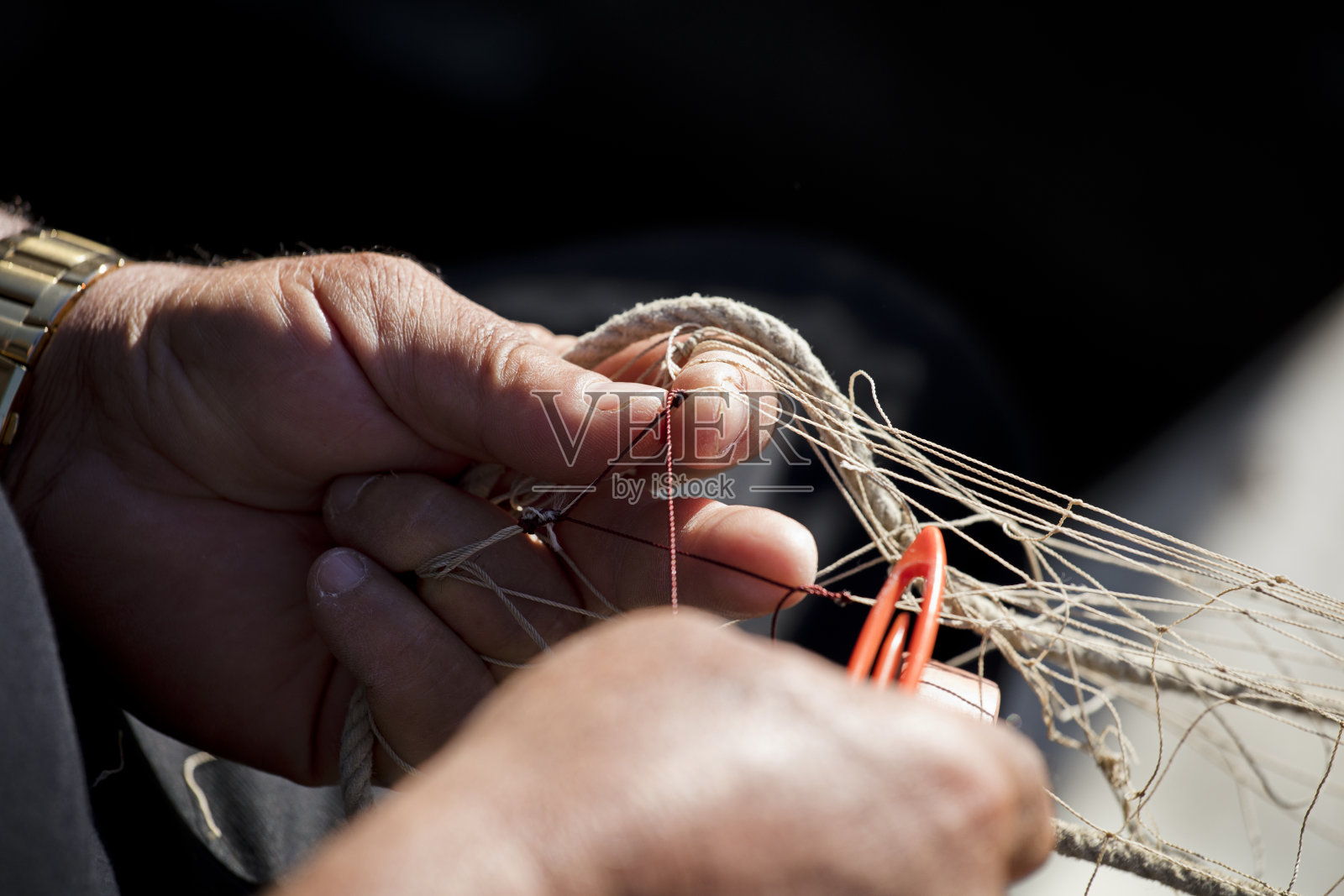 渔夫手中的渔网，他用针线编织和修补照片摄影图片