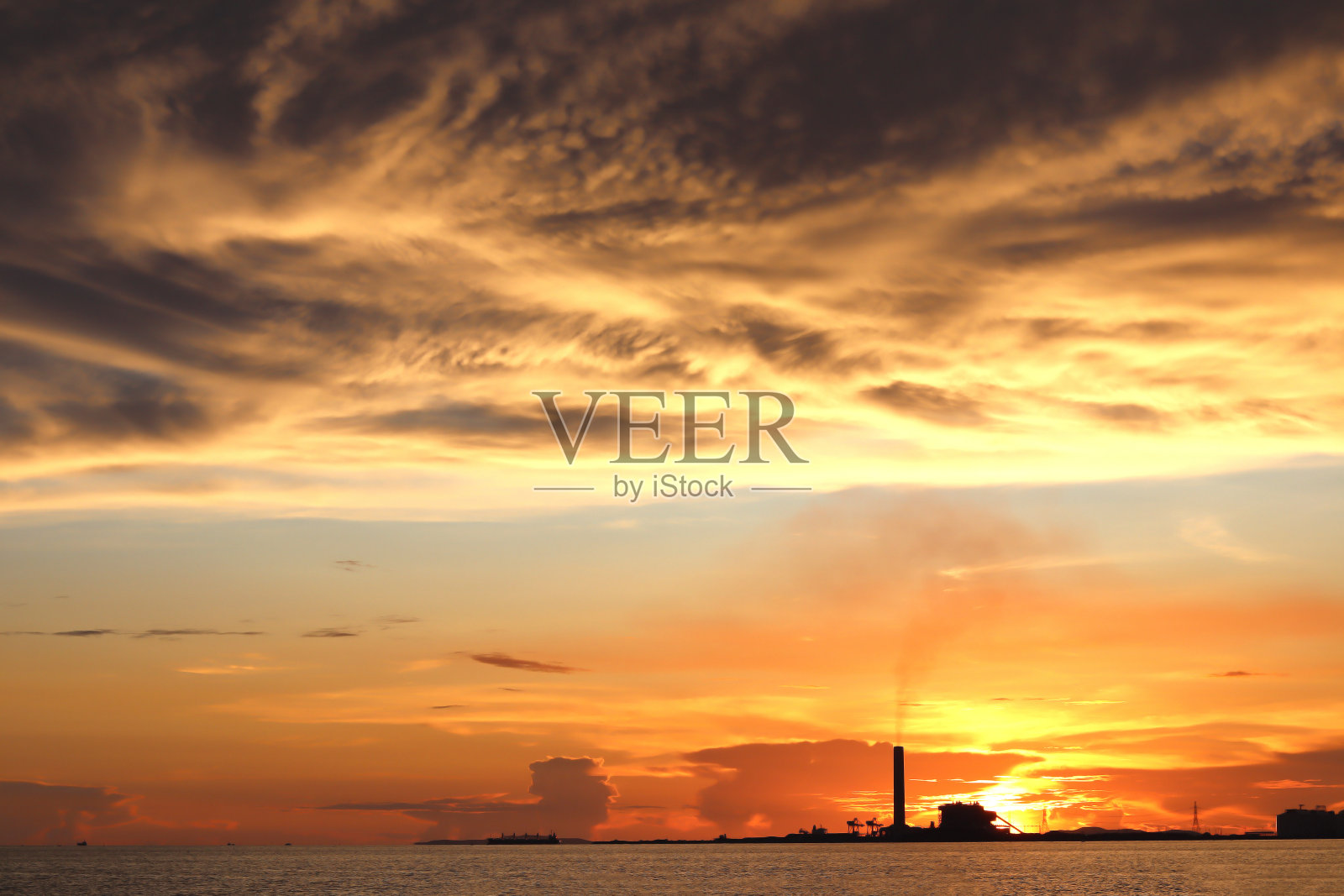 工厂排放的污染物。工业基地位于海边，黄昏日落。塔式起重机和施工现场的概念。空气中有很多污染物。照片摄影图片