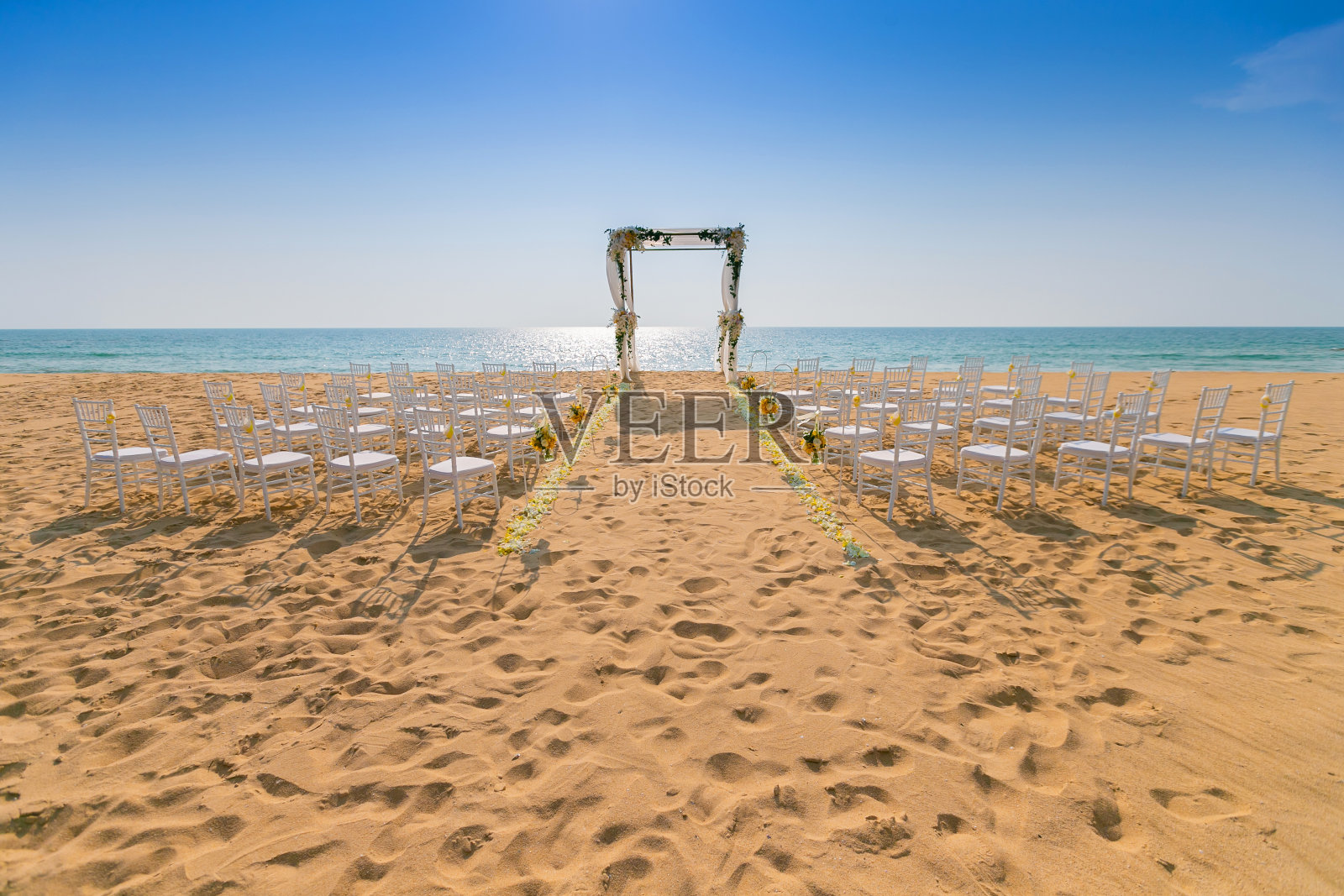 婚礼的拱门布置在沙滩上。天空是五彩缤纷的，椅子和走道上撒满了各种各样的花。照片摄影图片