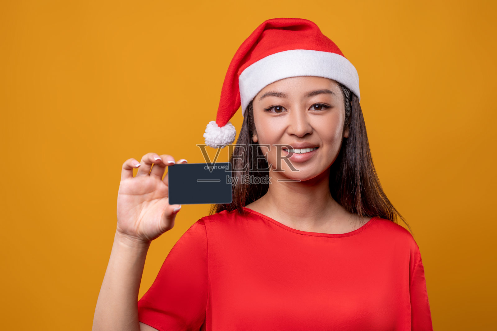 可爱的女人在红裙子和圣诞老人手里拿着信用卡照片摄影图片