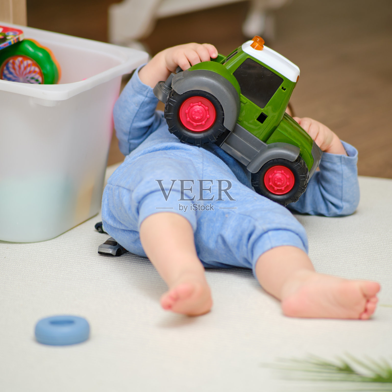 一个孩子光着脚躺在温暖的白色地毯上，特写。刚学会走路的小男孩躺在育儿室的地毯上玩耍。一岁零三个月的孩子照片摄影图片