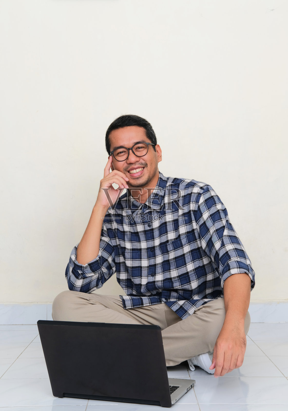 一名亚洲男子坐在他的笔记本电脑前的地板上，表情愉快照片摄影图片