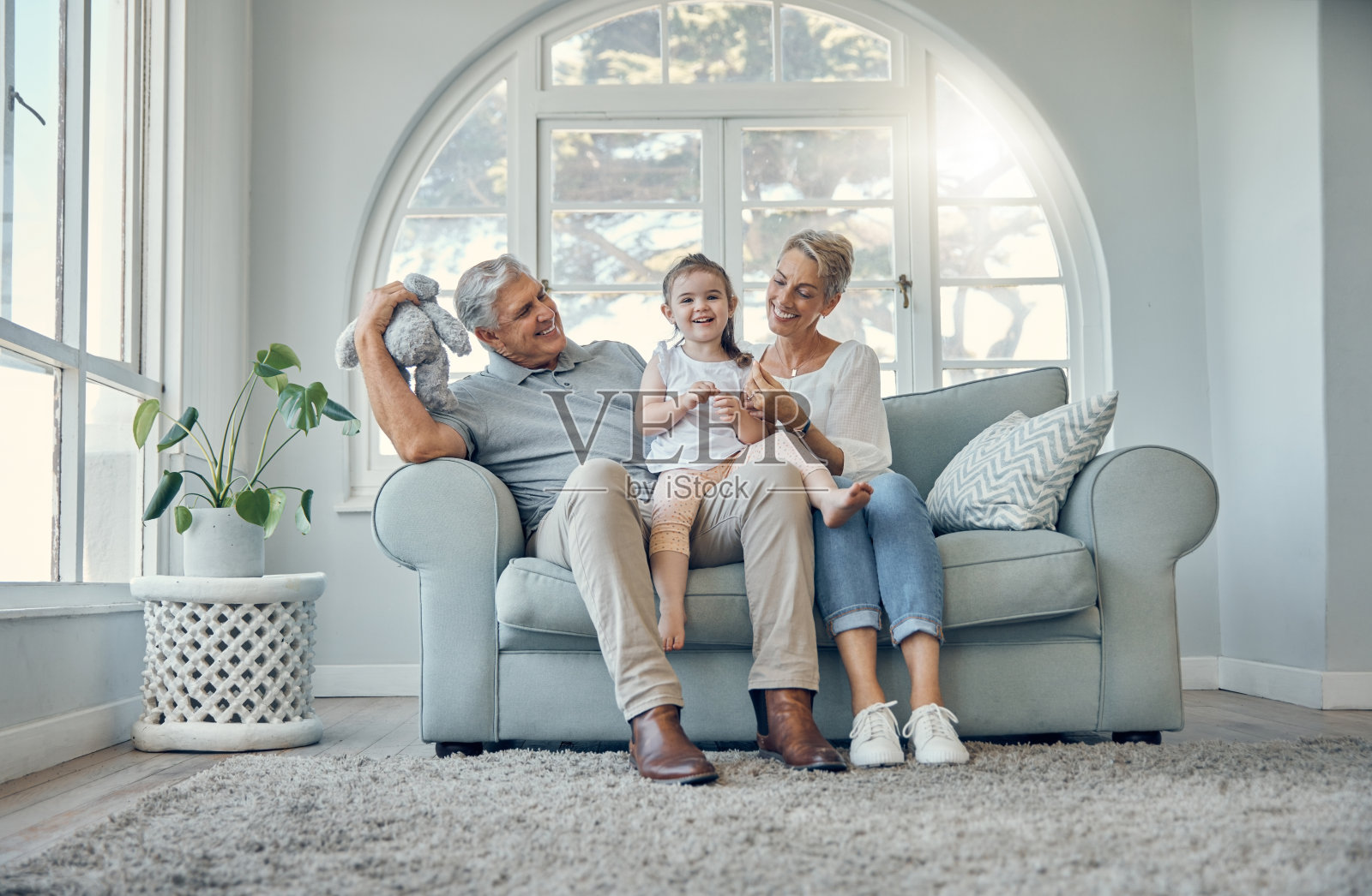 快乐，放松和爷爷奶奶带着一个孩子在客厅的沙发上在家里。快乐，祖母，祖父和女孩孩子一起坐在沙发上玩耍，建立联系，放松。照片摄影图片