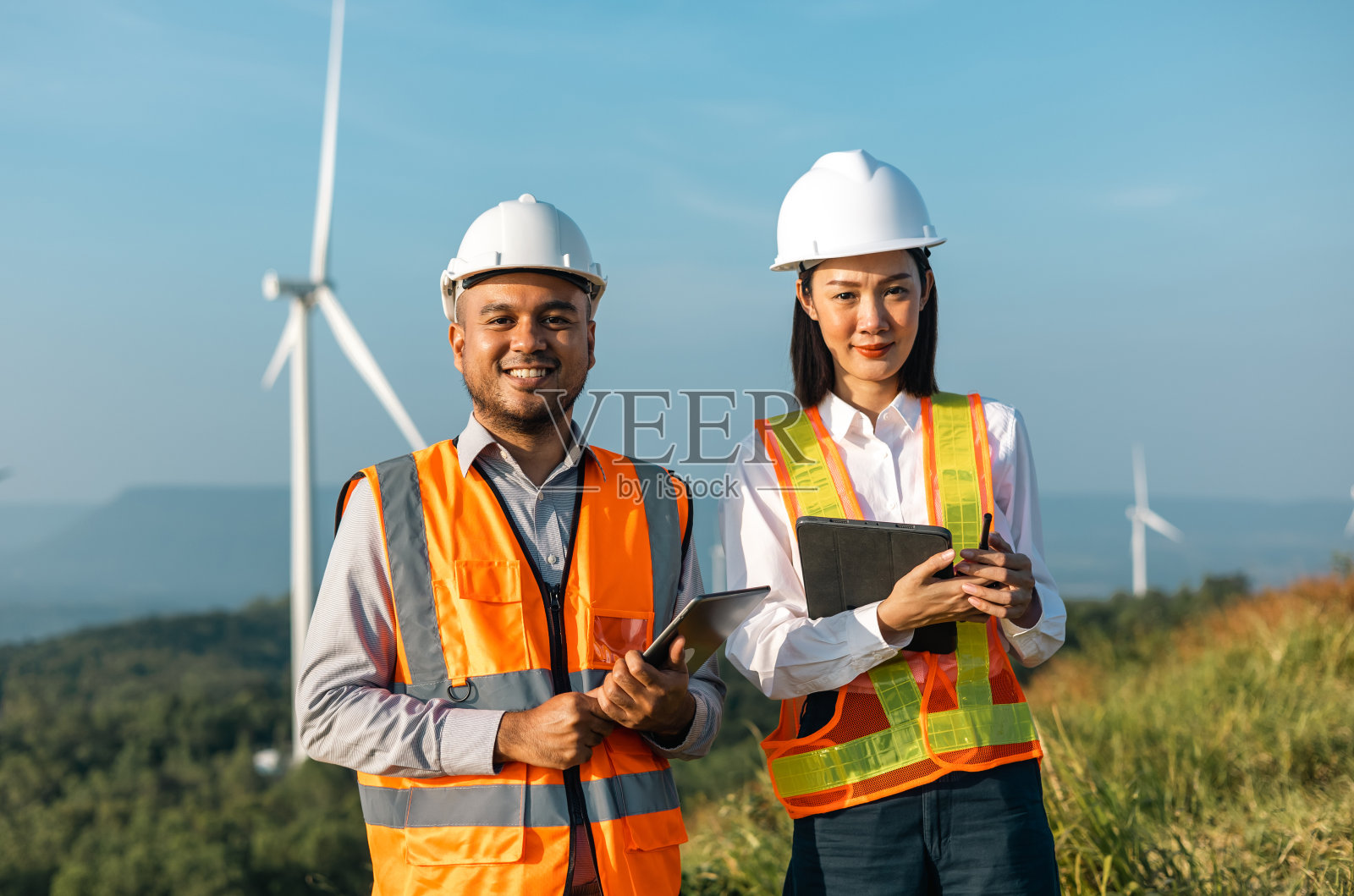 两名工程师在风车农场工作，生产电力和清洁能源。风力发电机是一种绿色替代能源。亚洲工程师检查控制电力照片摄影图片