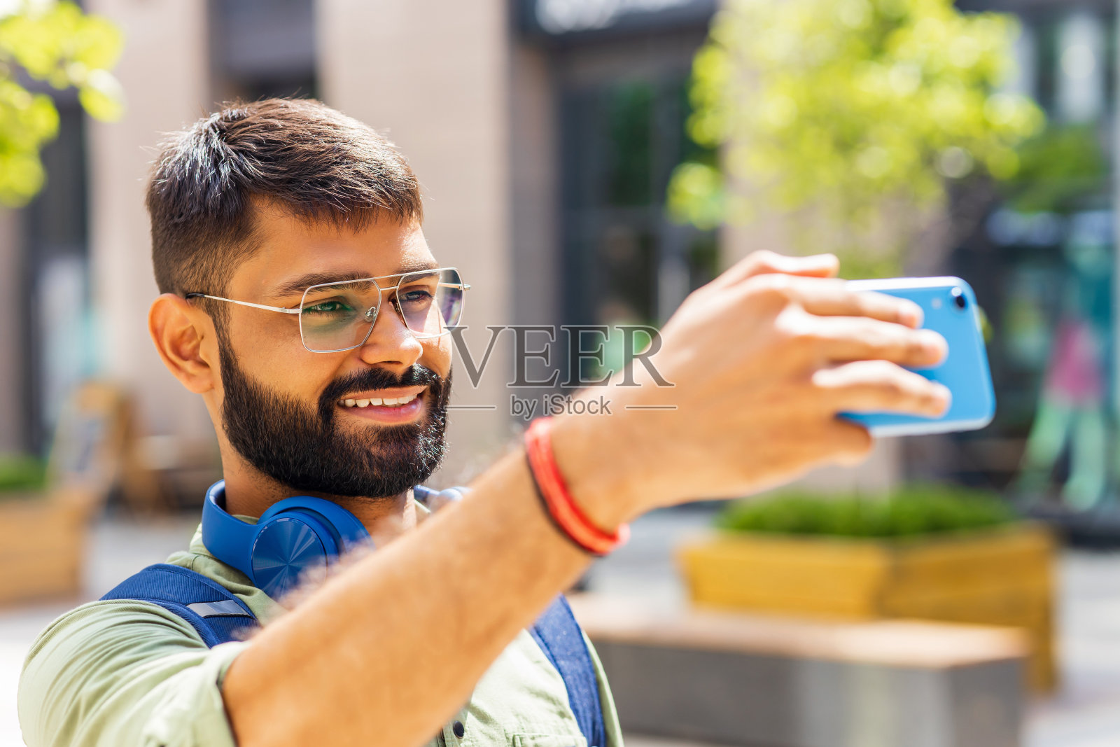 印度学生带着蓝色耳机和背包在阳光明媚的日子里用智能手机自拍照片摄影图片