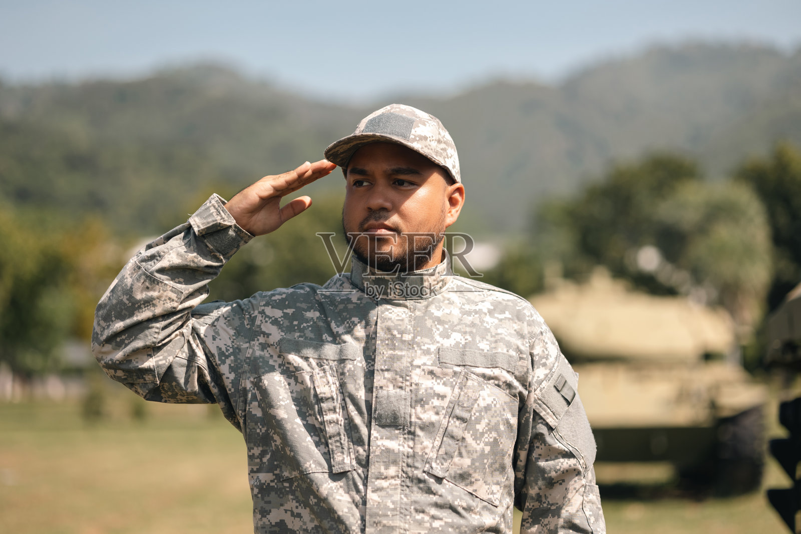 亚洲男子特种部队士兵敬礼站在外地任务。在战争状态下，身着军装的军队守卫者站在战斗坦克旁。照片摄影图片
