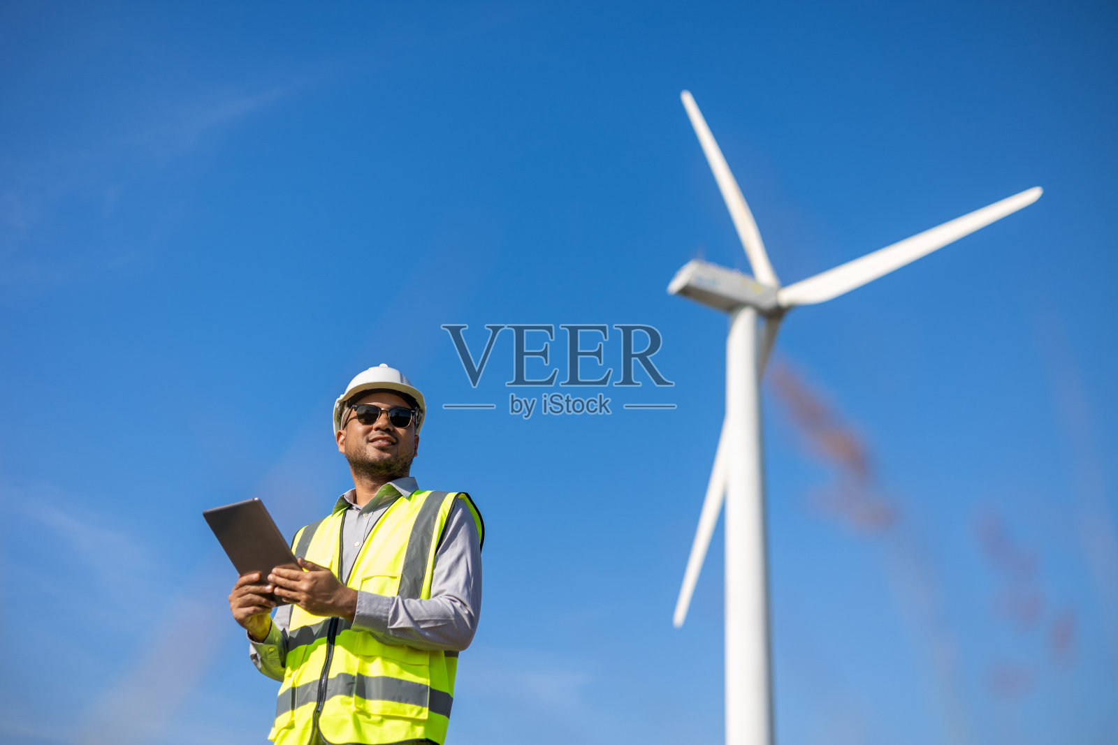 印度工程师在风车农场用平板电脑发电清洁能源。风力发电机是一种绿色替代能源。亚洲工程师检查控制电力照片摄影图片