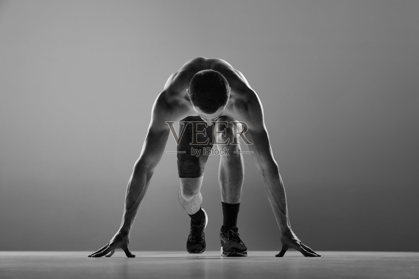 力量和能量。肌肉发达的运动员，跑在起跑线孤立灰色背景。运动美理念。黑白肖像。单色照片摄影图片