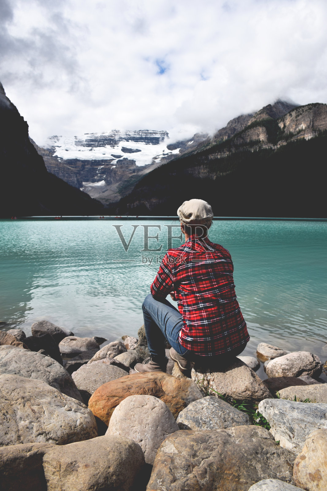 穿着红色格子衬衫的女人坐在岩石上欣赏湖和山的景色照片摄影图片