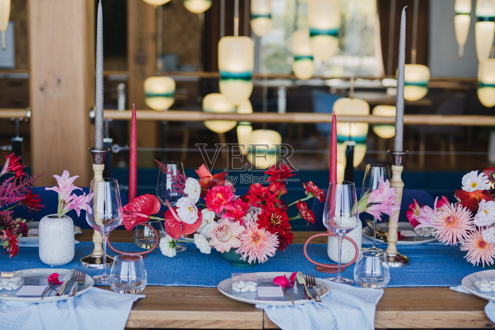 婚宴上的餐桌摆设。有美丽的花朵和绿色植物的花卉作品，蜡烛，装饰好的桌子上的摆设和盘子。照片摄影图片