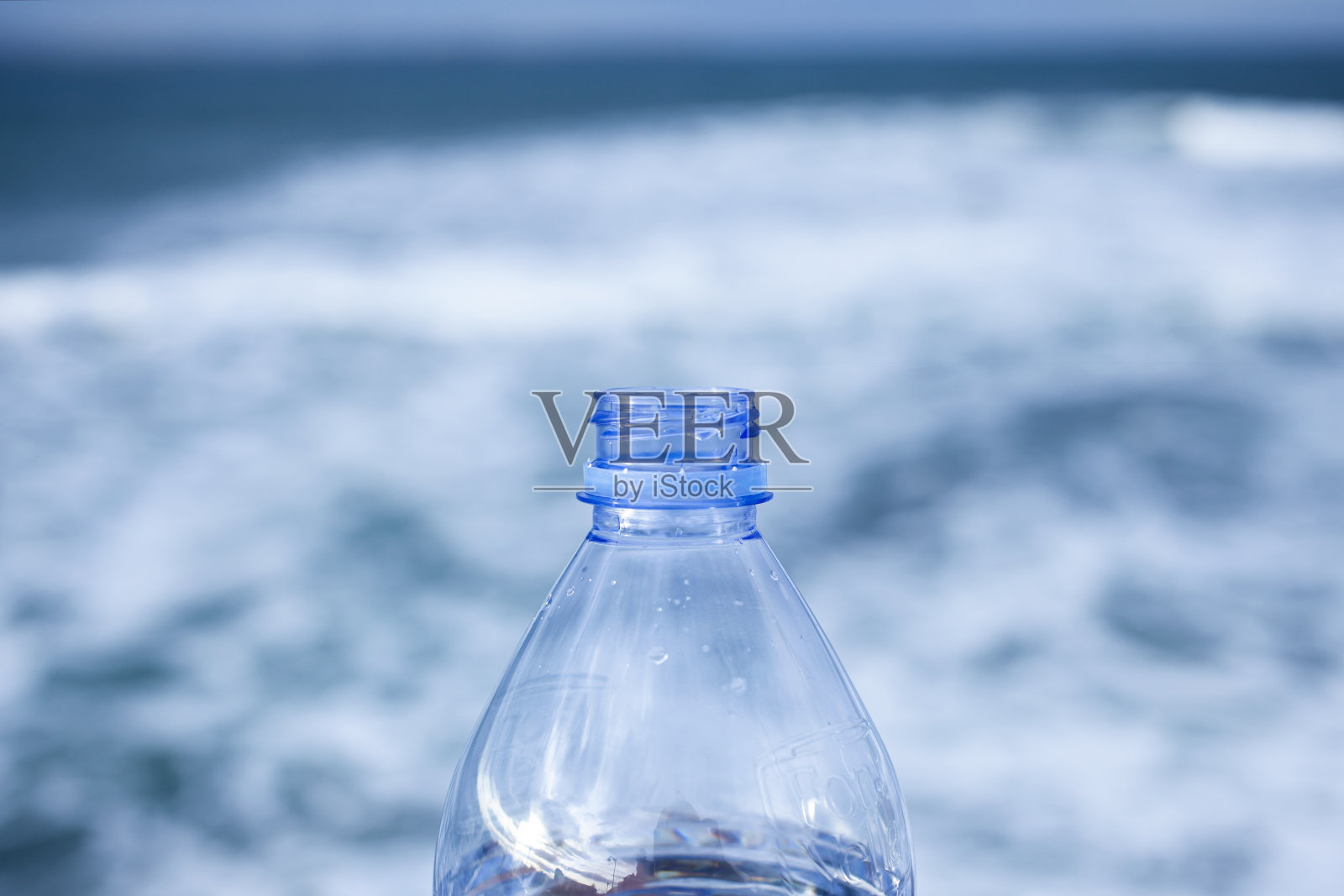 特写的透明打开塑料瓶没有盖子与选择性聚焦和散焦自然海洋背景。塑料回收概念。没有螺旋盖的塑料瓶。照片摄影图片