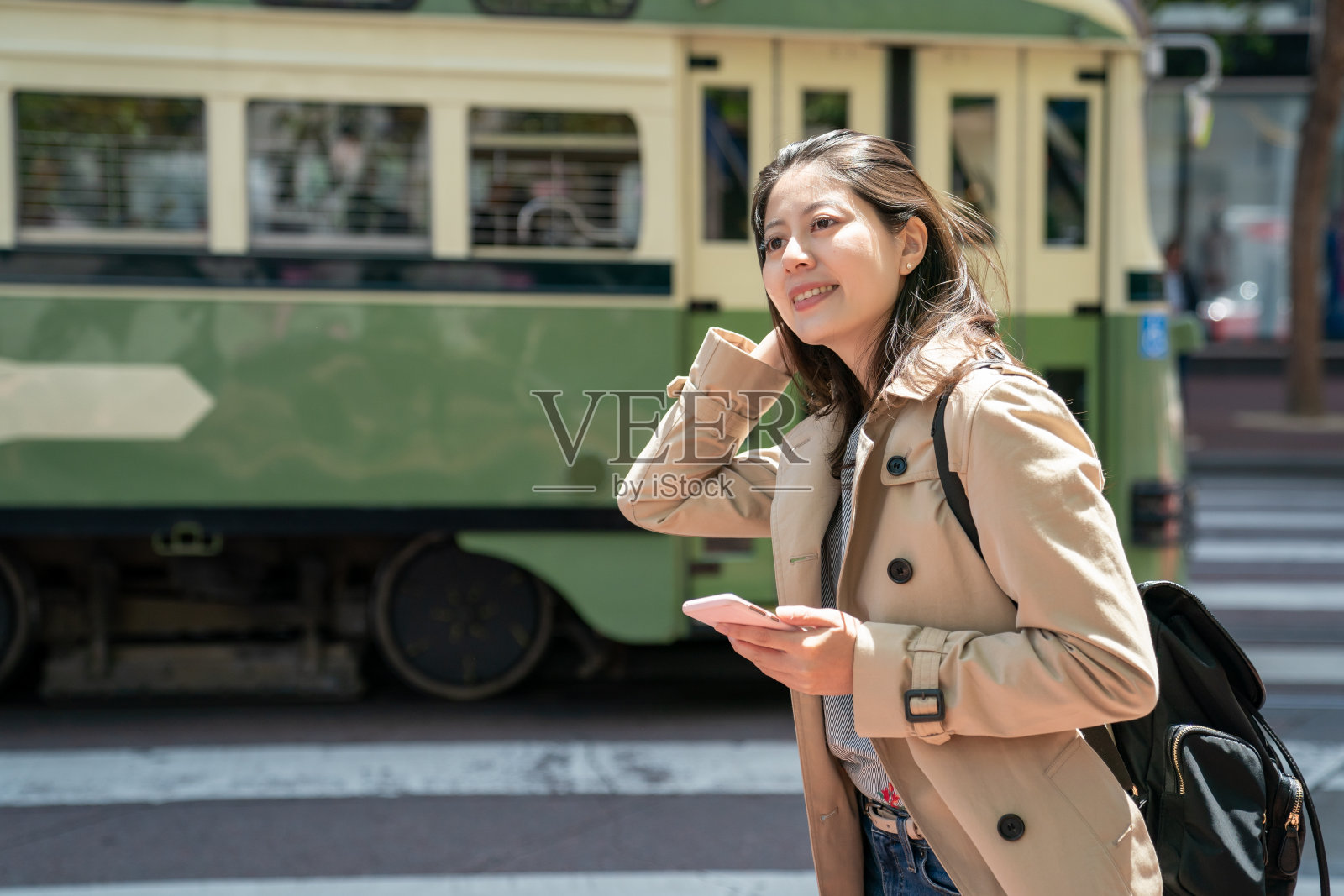 快乐的亚洲中国女性游客在微风中看向远处在美国加州旧金山的路边。她的手在微风中摸着头发，背景是一辆公共汽车停在那里照片摄影图片