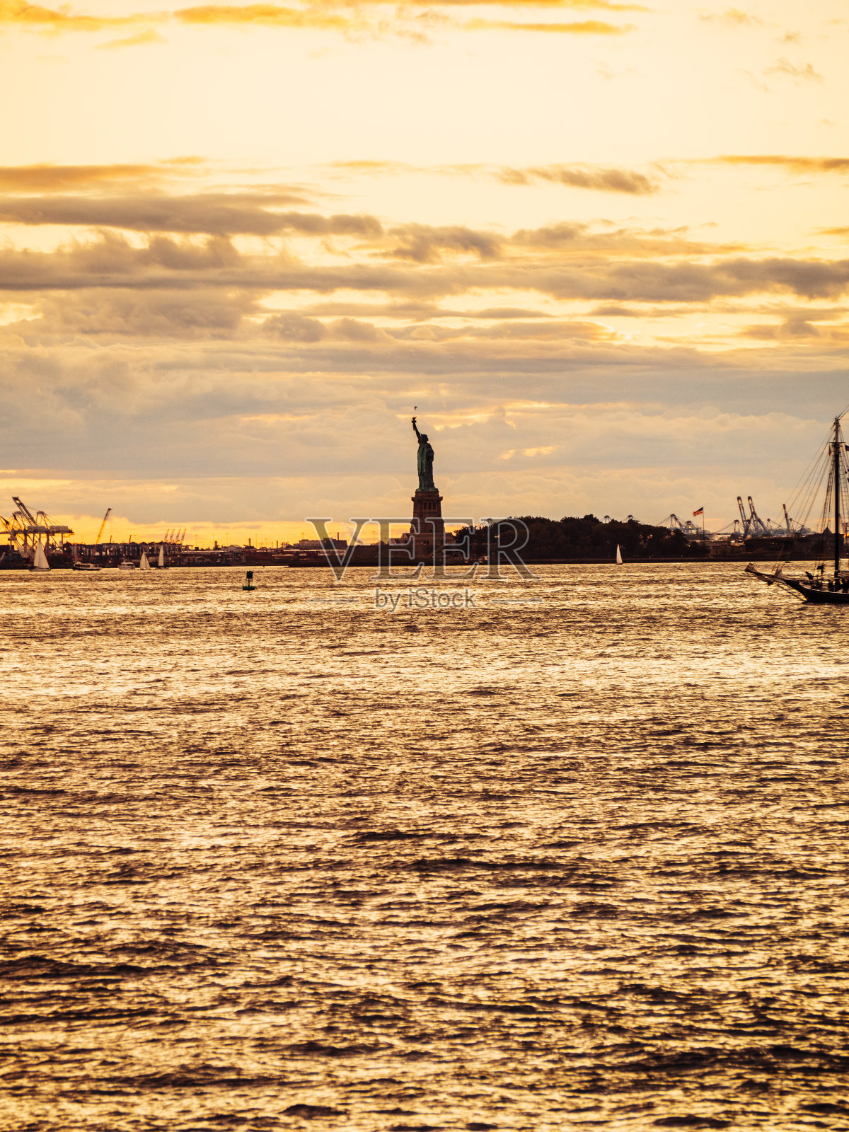 自由女神像的剪影映衬着纽约市金色多云的天空照片摄影图片
