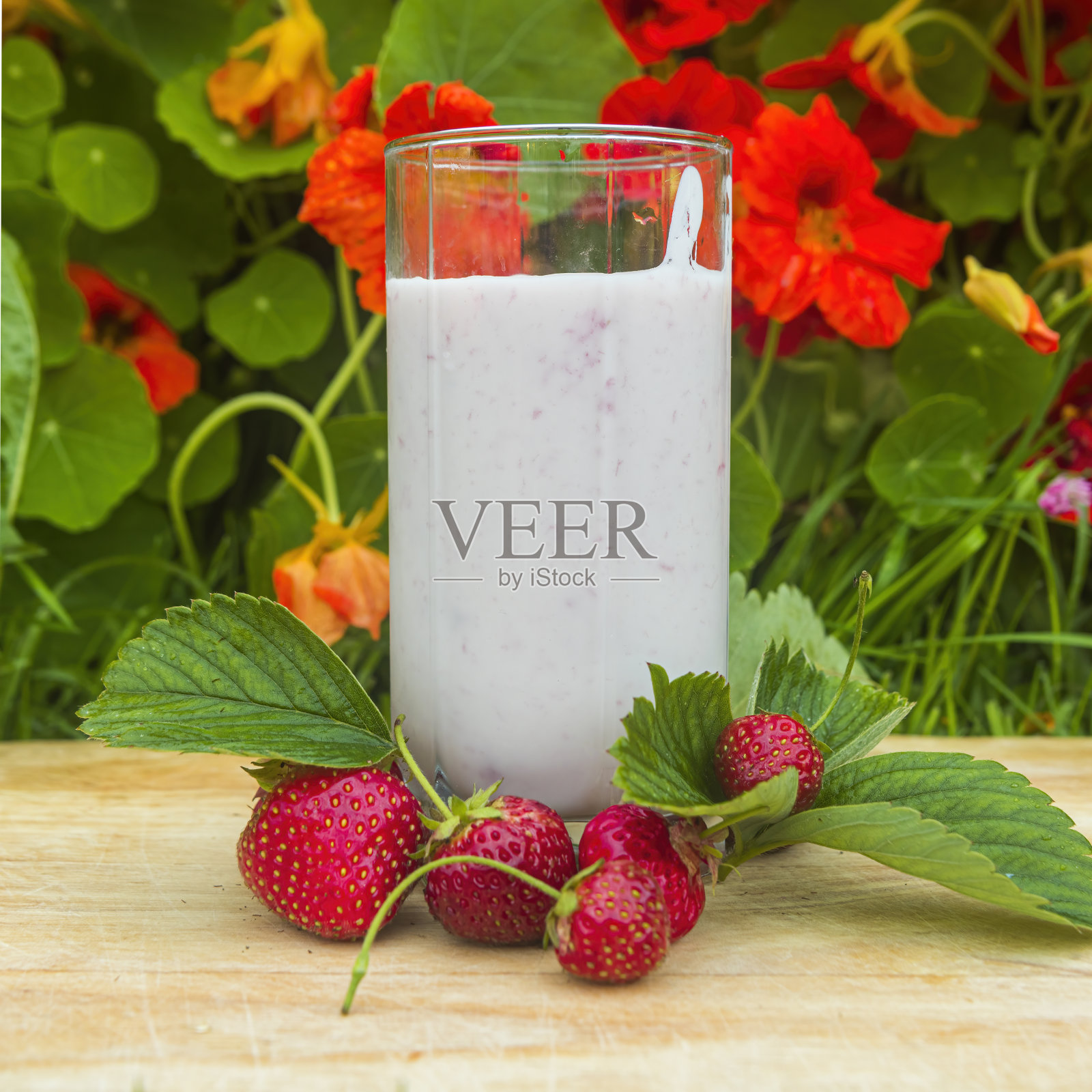 一杯草莓酸奶的背景是树叶，新鲜的草莓躺在旁边照片摄影图片