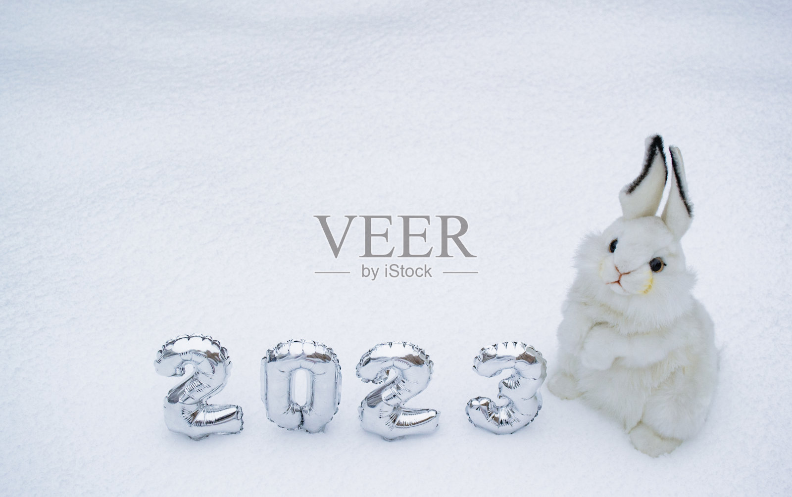 白色毛茸茸的兔子玩具，白色的雪背景上有2023年的银色数字。副本的空间。2023年中国新年的标志照片摄影图片