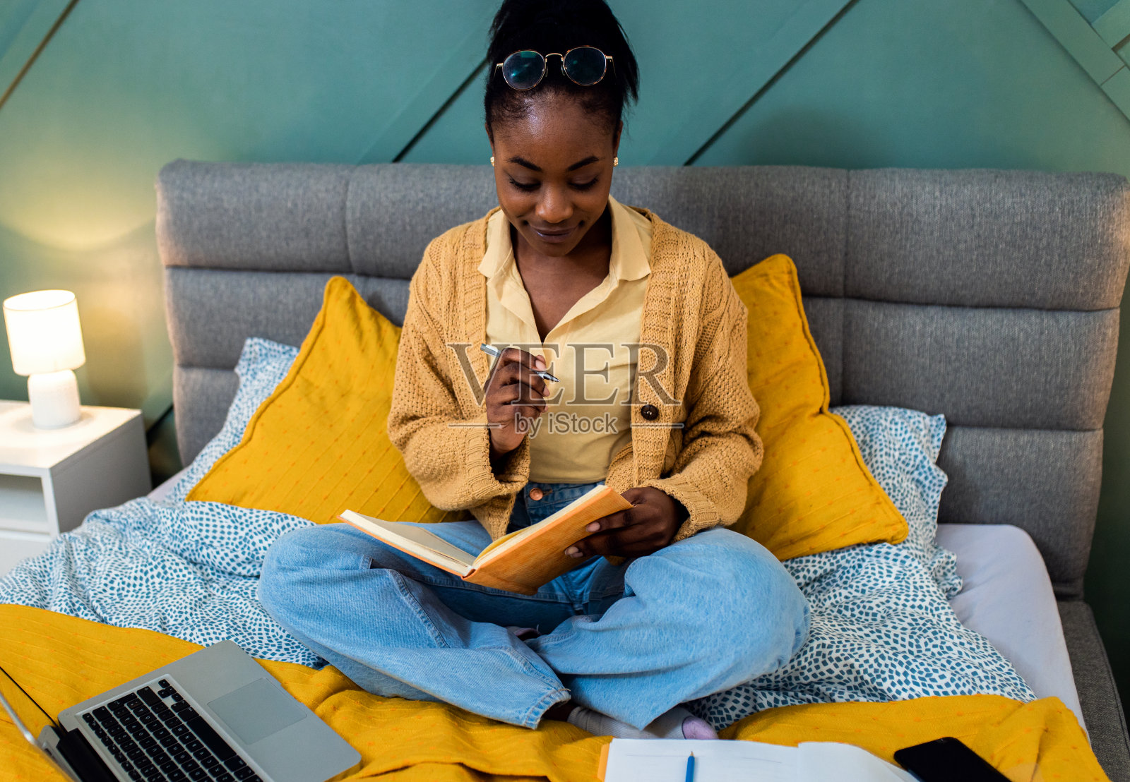 年轻的非裔美国妇女坐在卧室的床上用笔记本电脑学习。照片摄影图片